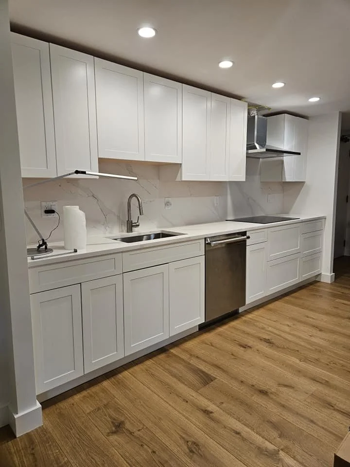 Modern kitchen with white cabinets, marble backsplash, stainless steel dishwasher, single basin sink, and wooden flooring.