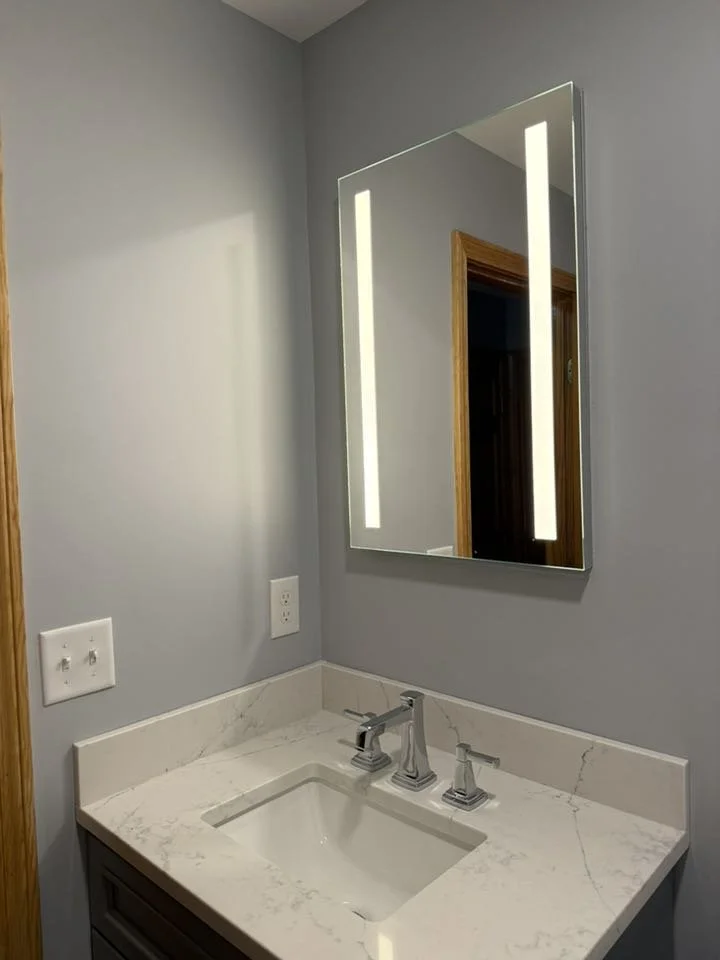 Bathroom vanity with marble countertop, rectangular undermount sink, and modern silver faucet, with a wall-mounted mirror illuminated by vertical LED lights.