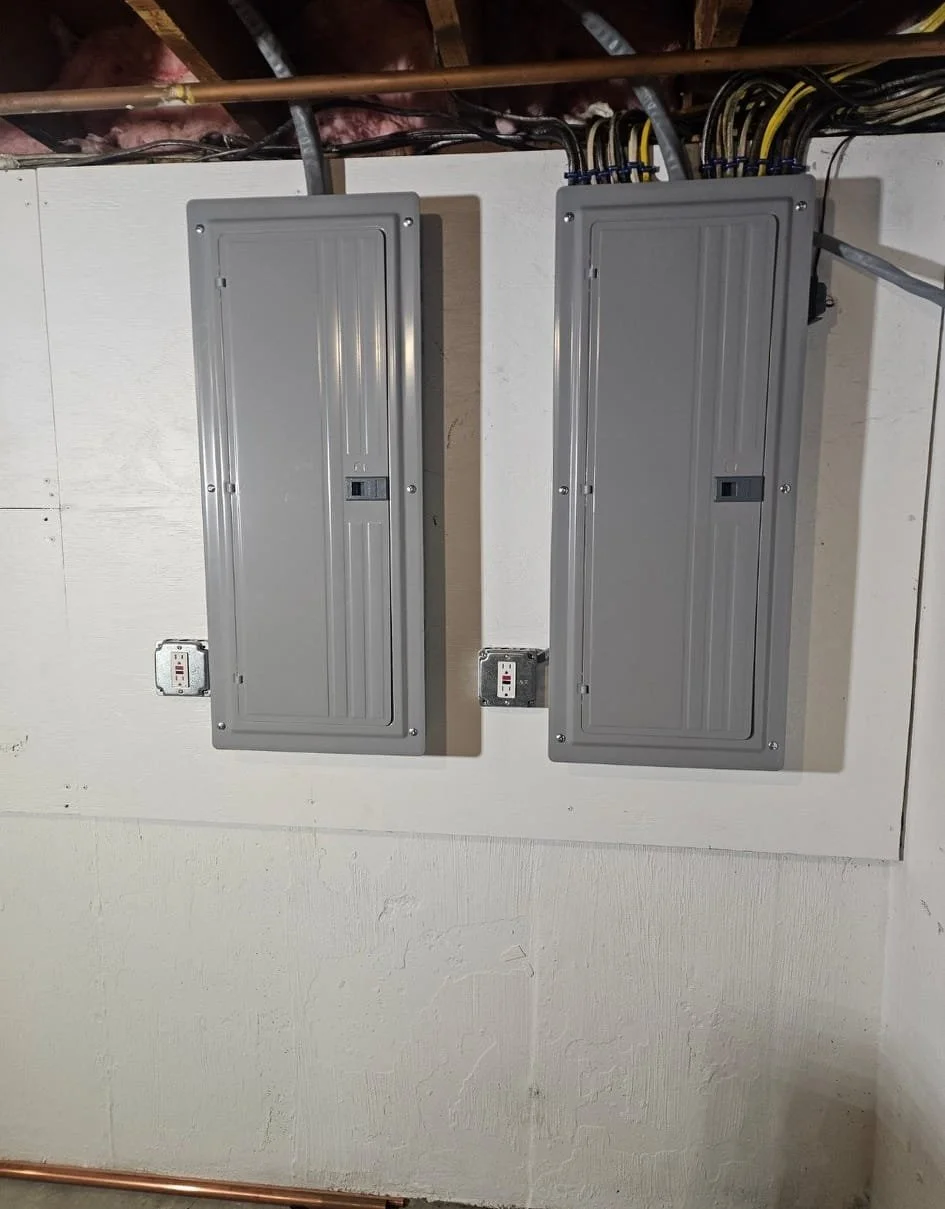 Two gray electrical breaker boxes mounted on a white wall, with wiring coming from the ceiling.