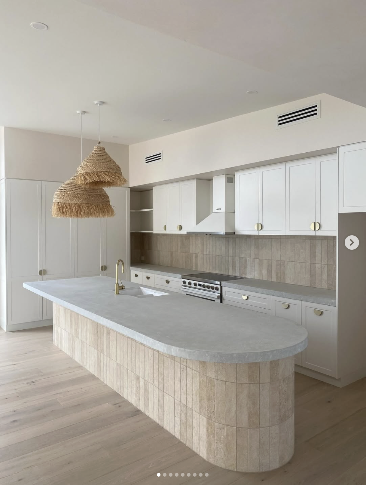 Modern kitchen with white cabinetry, beige tile backsplash, a large marble island with a gold faucet, and a woven pendant light.