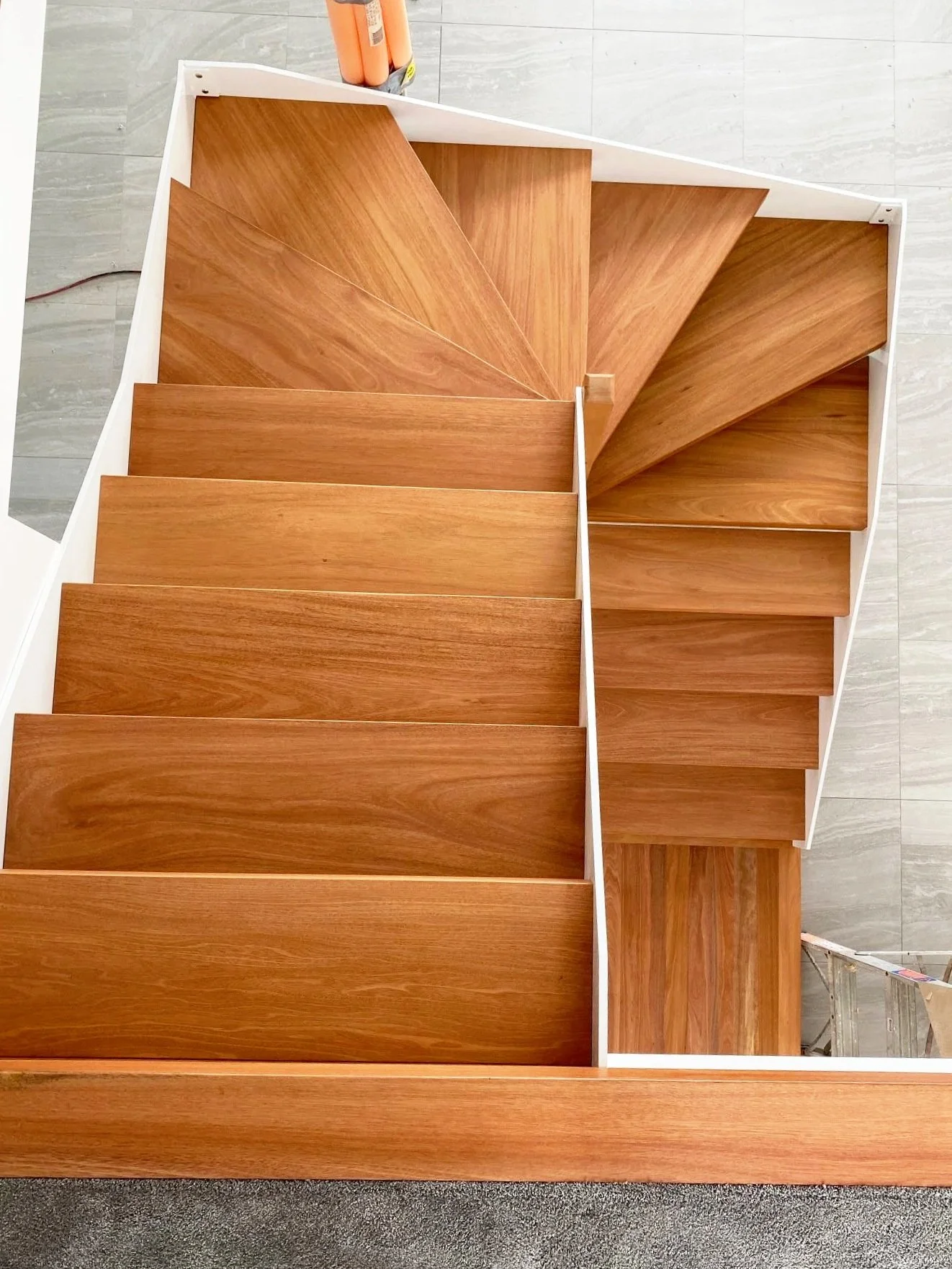 Top view of wooden staircase with angled steps, white safety railing, and gray tiled floor.