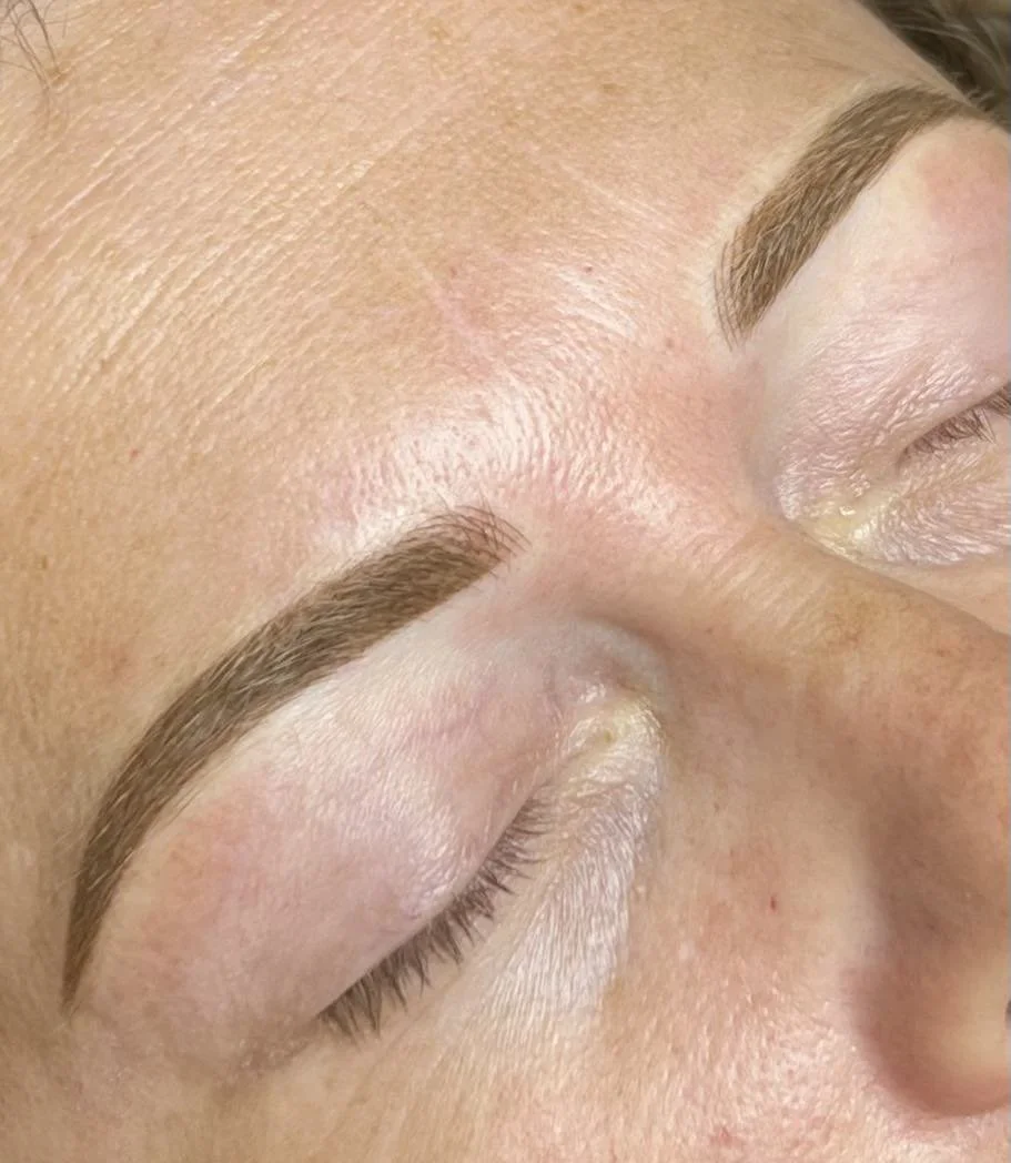 Close-up of a person's face with eyes closed, showing freshly tattooed eyebrows.