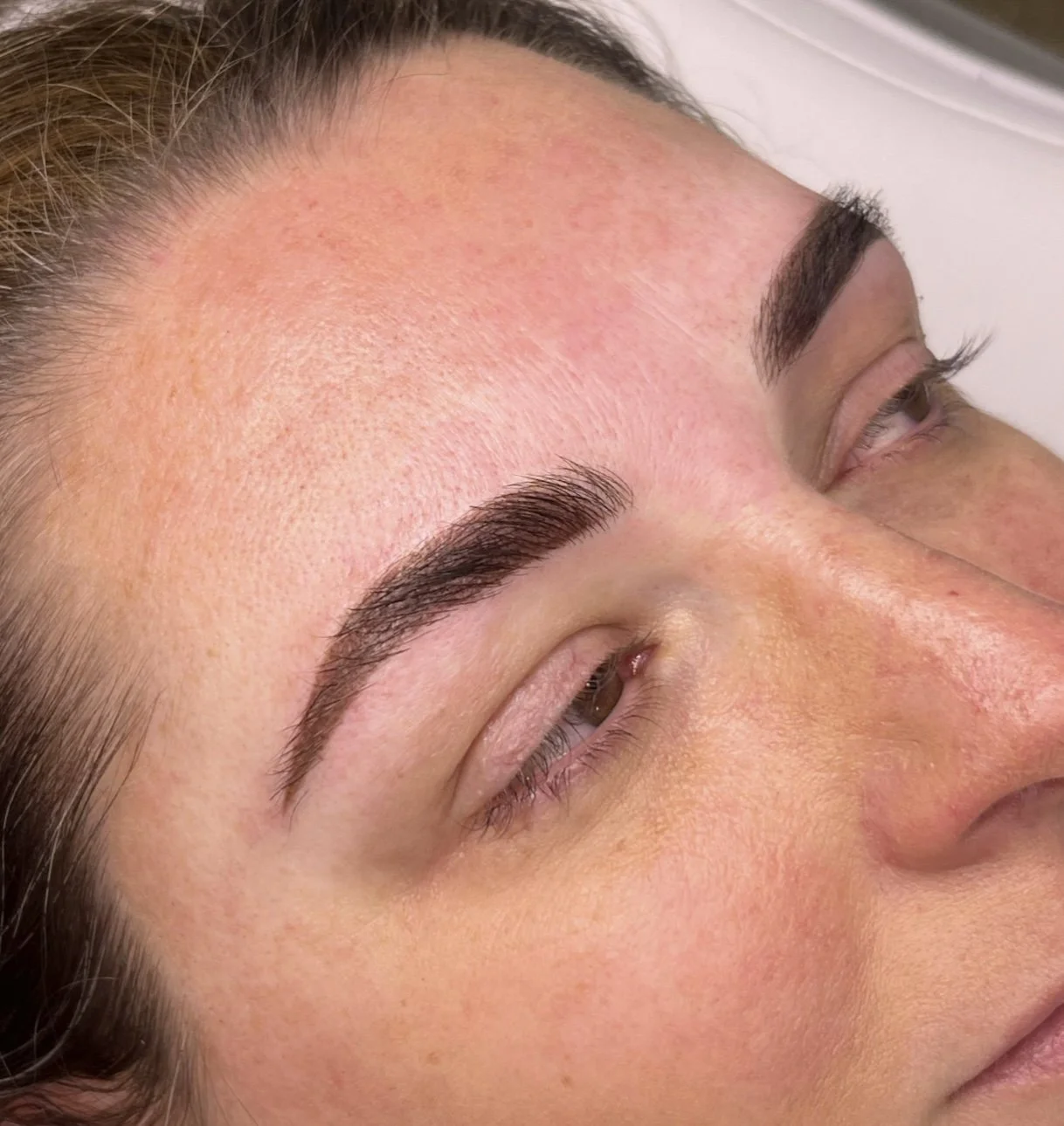 Close-up of a woman's face showing freshly tattooed and shaped eyebrows.