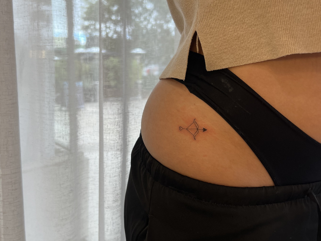 Client image of fine line tattoo of bow and arrow on hip by Banksia and Blade