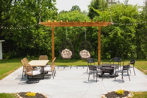Backyard patio at the Villa at Ramble Creek, featuring outdoor dining, fire pit seating, hanging egg chairs, and a wooden pergola surrounded by greenery.
