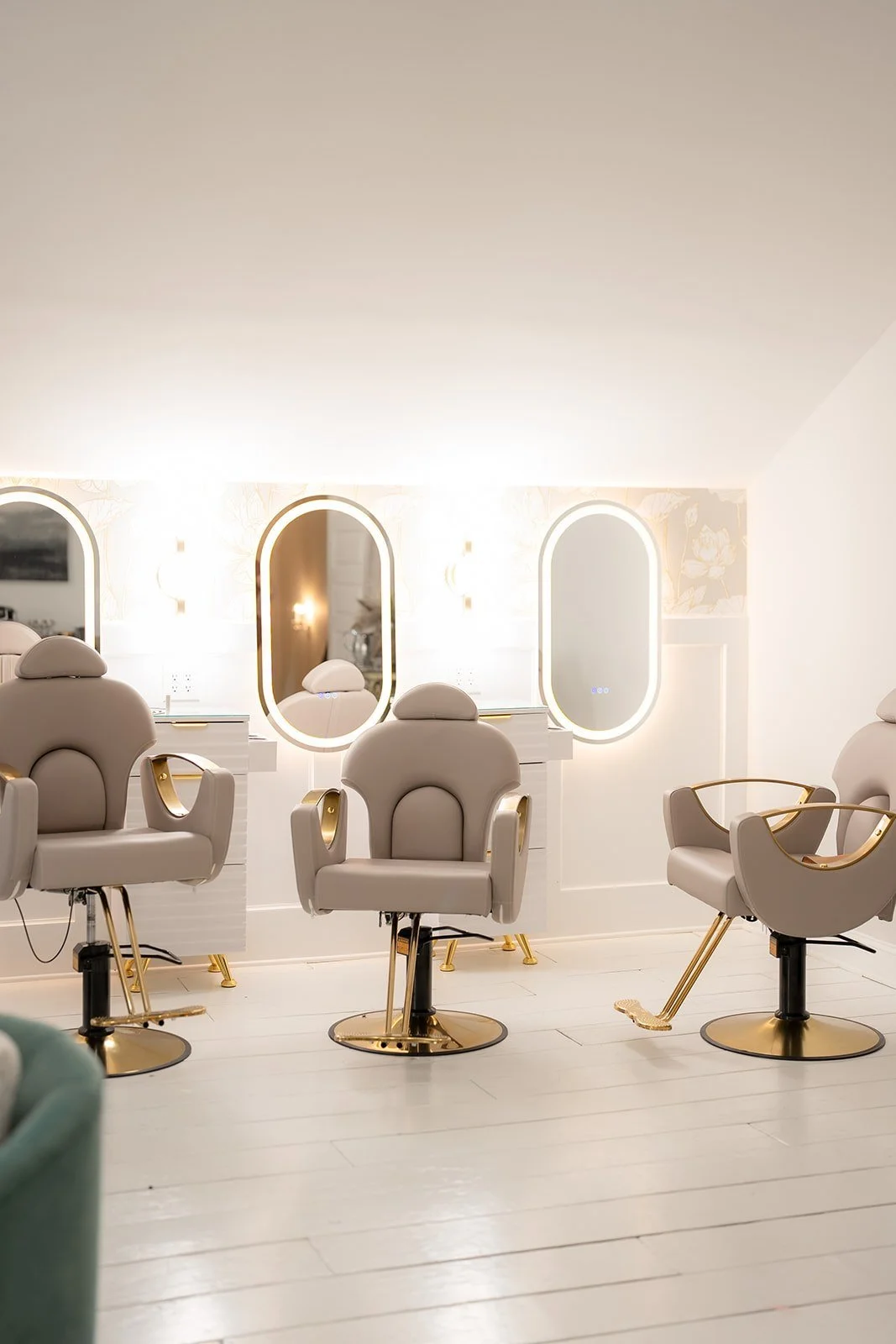 Elegant bridal suite getting ready area with three beige styling chairs and oval illuminated mirrors on a white wall.