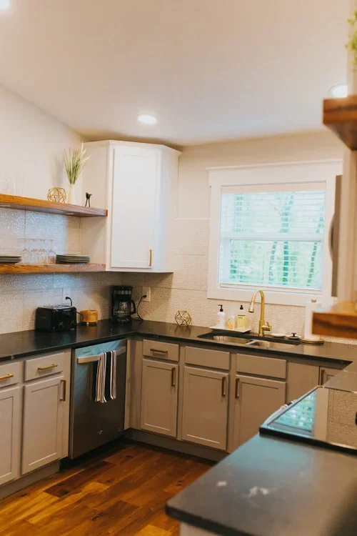 Kitchen with gray cabinets, black countertops, a window above the sink, and wooden shelves. One of three accommodations at Ramble Creek Tennessee wedding venue with on-site lodging.