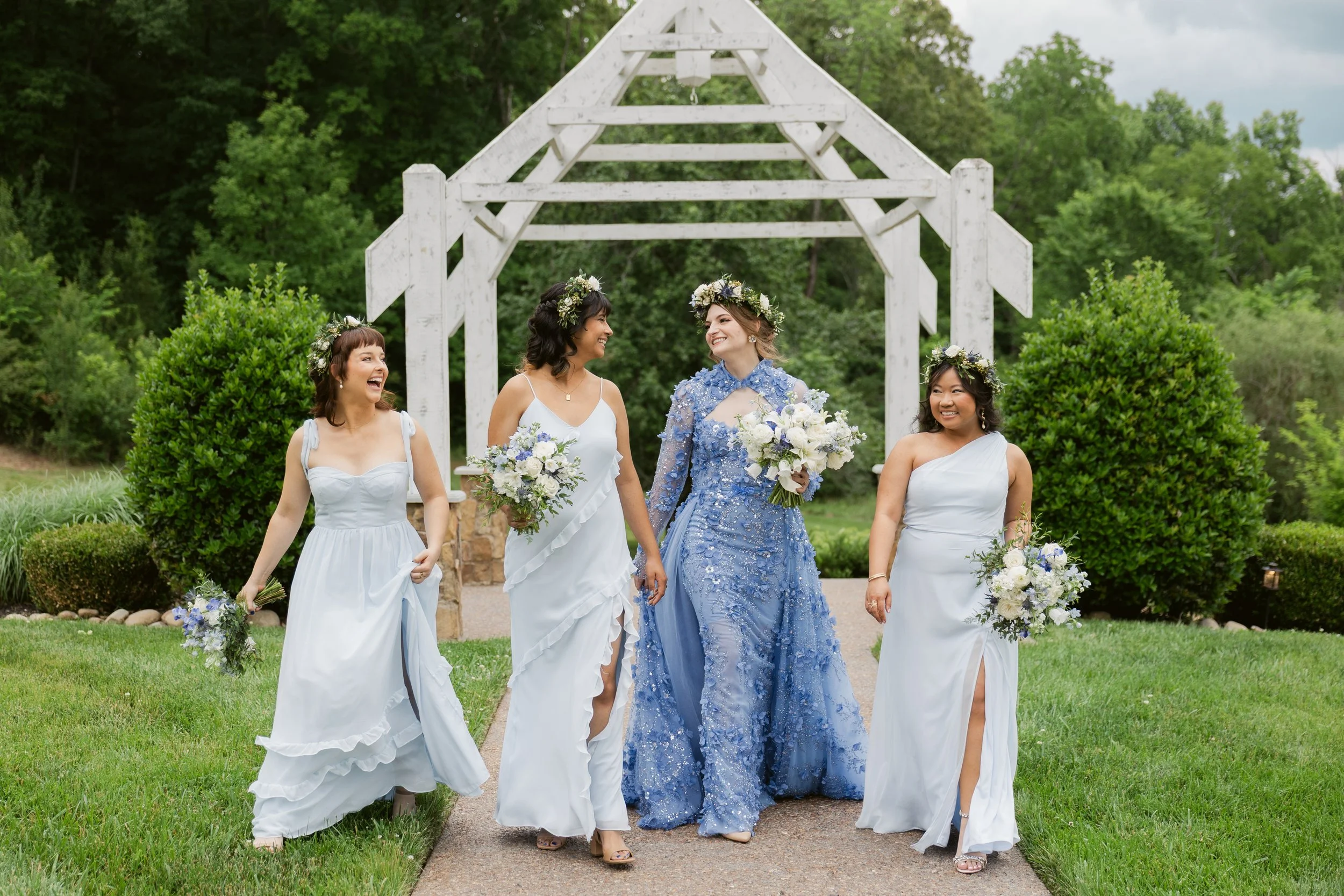 Bride in a blue floral wedding dress walking with bridesmaids at the outdoor ceremony arbor at Ramble Creek, an all-inclusive East Tennessee wedding venue in Athens TN.