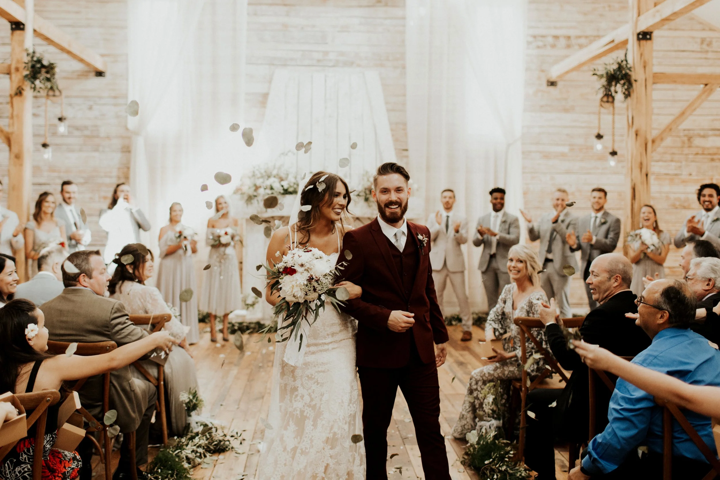 A bride and groom walking down the aisle at their Ramble Creek indoor wedding ceremony inside a rustic venue with wood walls and beams, surrounded by seated guests and family.