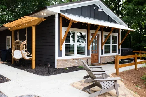 A small modern house with black siding, large windows, wooden accents, and a front porch with chairs, surrounded by trees. One of three accommodations at Ramble Creek Tennessee wedding venue with on-site lodging.