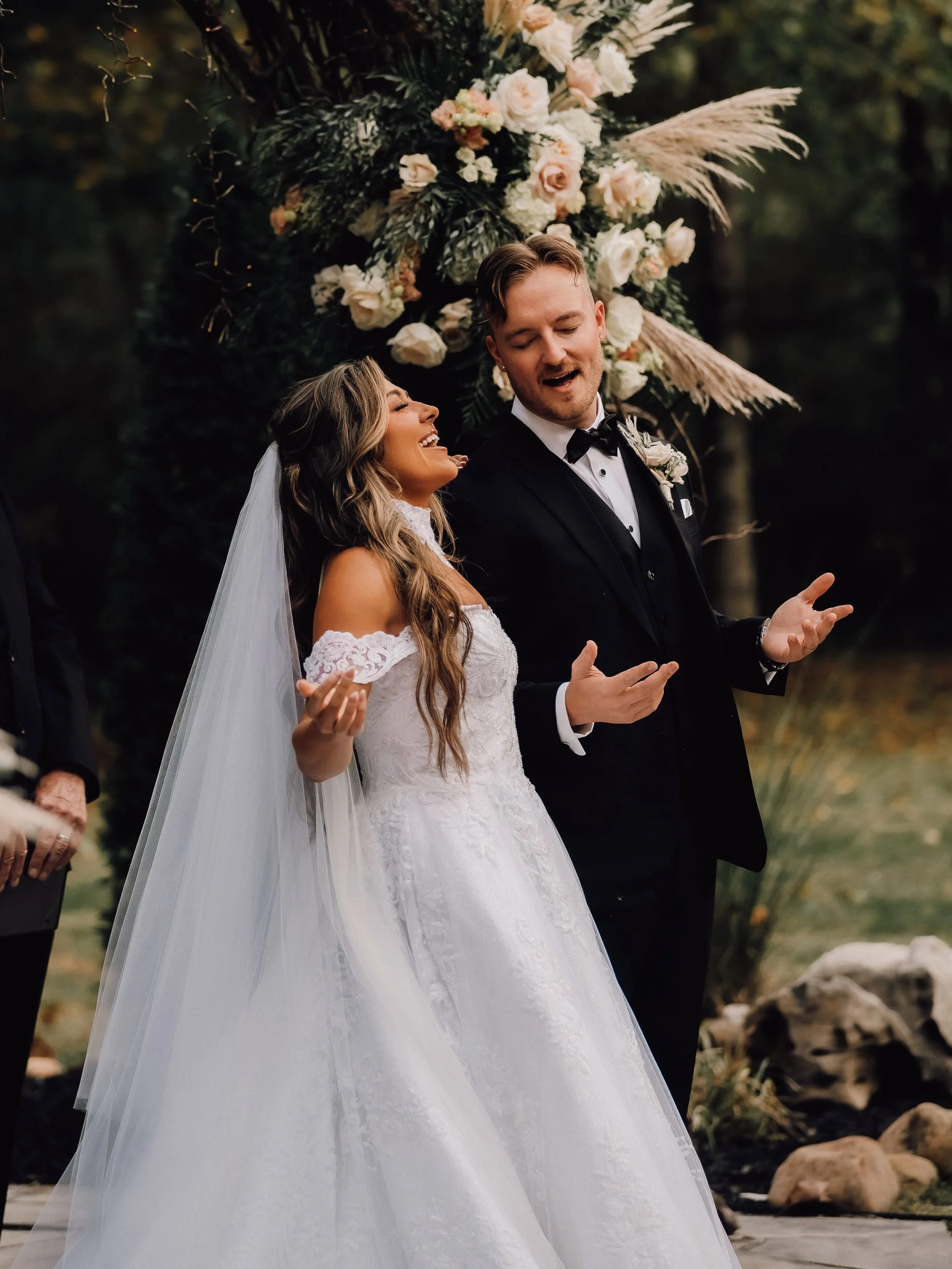 Kara Lewis and West Webb sing with eyes closed and palms raised during worship at their wedding ceremony beneath Ramble Creek’s flower-adorned Vine Arbor