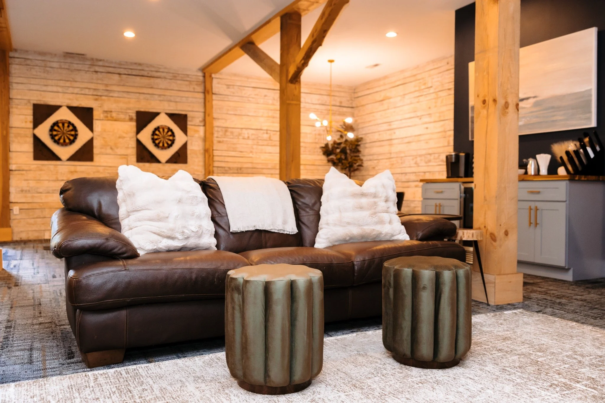 Groom's getting ready area at Ramble Creek wedding venue with a brown leather sofa, white pillows, wooden accents, dartboard on the wall, and a kitchen area in the background.
