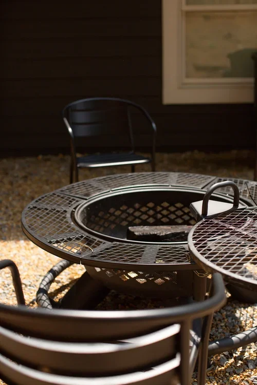 Outdoor patio with metal table and chairs, and a fire pit in a backyard at dusk.