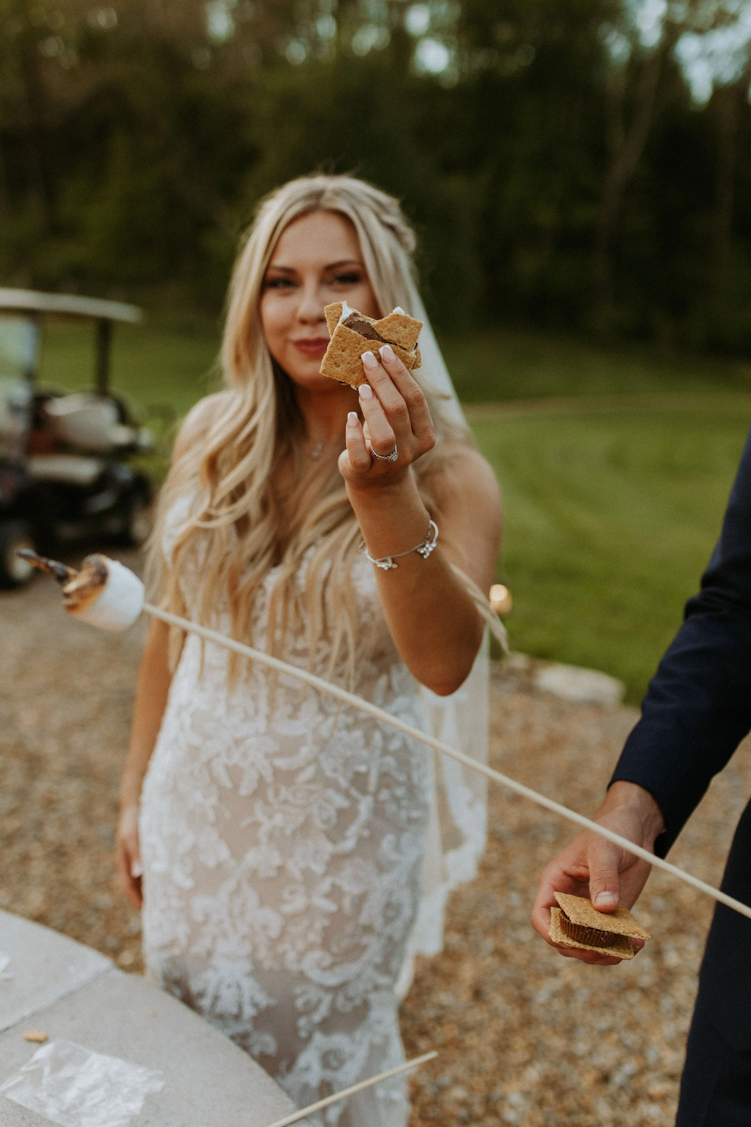 Bride at Ramble Creek fire pit holding a s'more up to the camera after her all-inclusive wedding