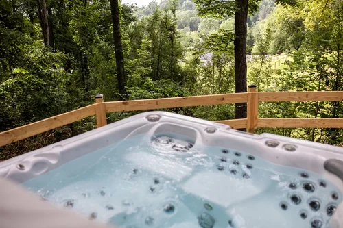 A hot tub with bubbling water outdoors surrounded by trees and a wooden railing. One of three accommodations at Ramble Creek Tennessee wedding venue with on-site lodging.