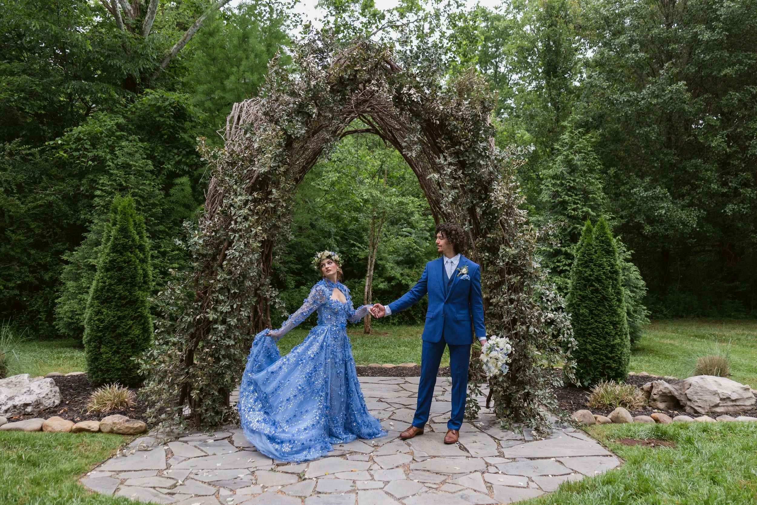 Bride in a blue floral wedding dress and groom in a blue suit beneath the ceremony vine arbor at Ramble Creek, an all-inclusive East Tennessee wedding venue in Athens TN.