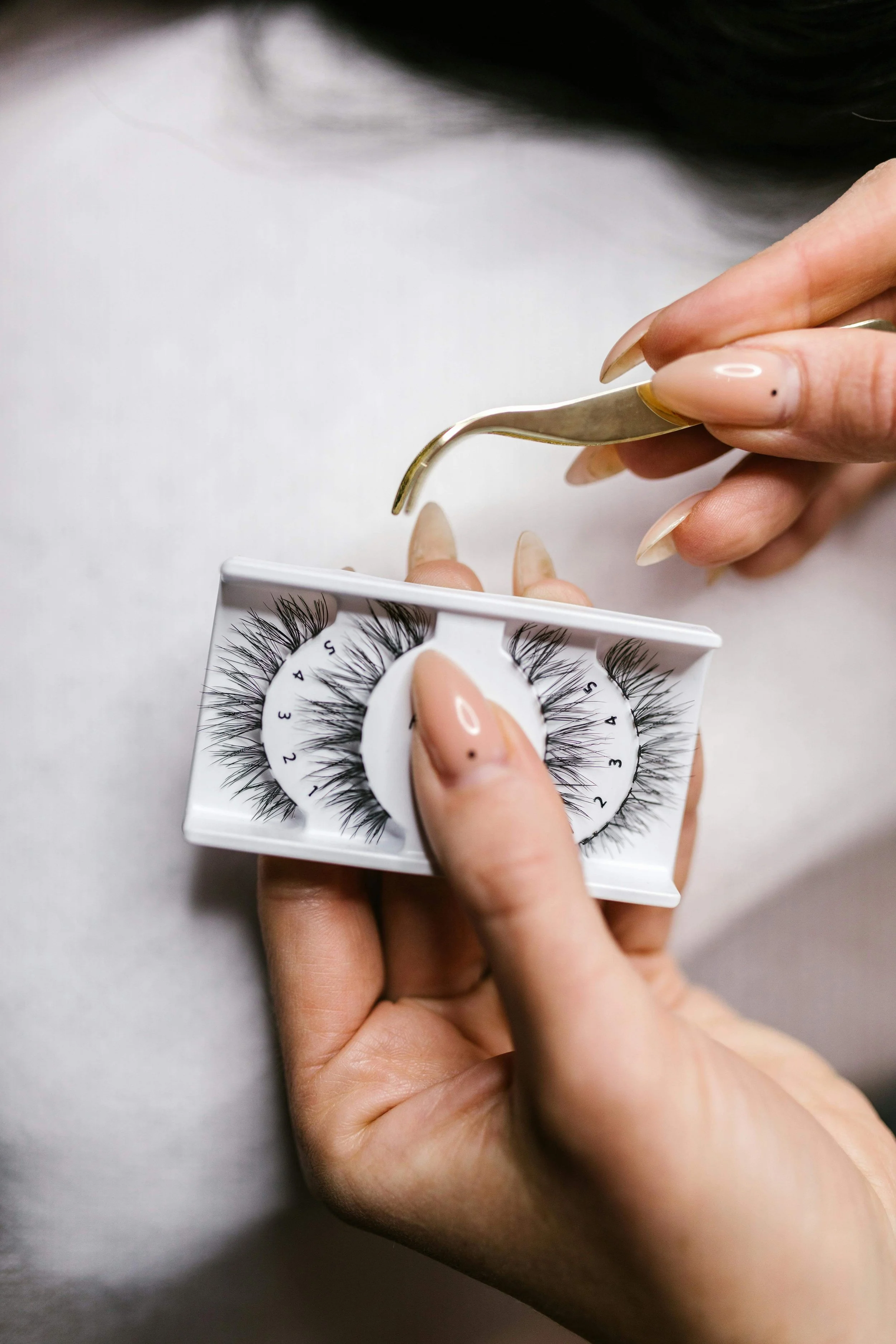 Close-up of false eyelashes being lifted from a tray with tweezers during bridal makeup preparation