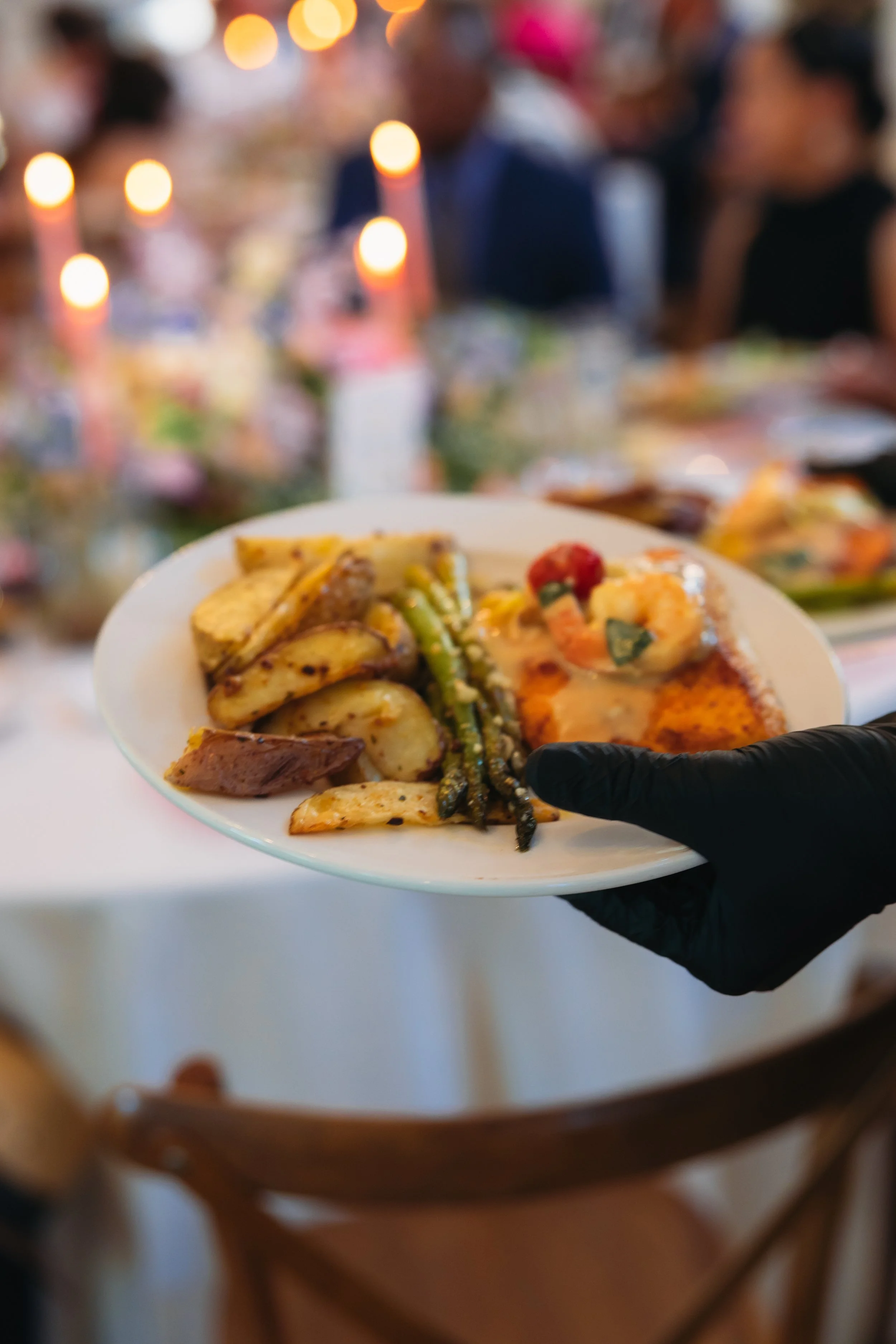 Ramble Creek server in a black glove holding a plate of food at Tennessee wedding reception with blurred people and warm lighting in the background.