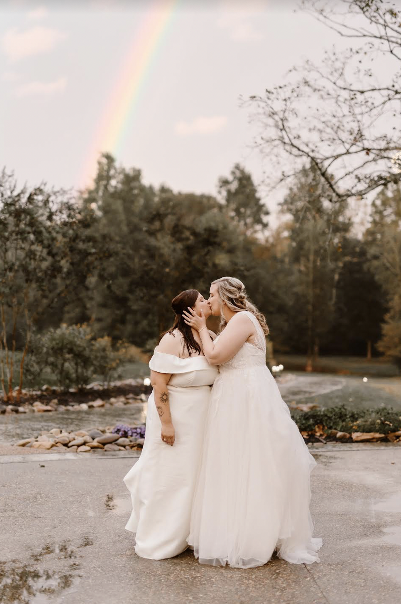 Two brides kissing in their edding dresses after a storm with a rainbow behind them