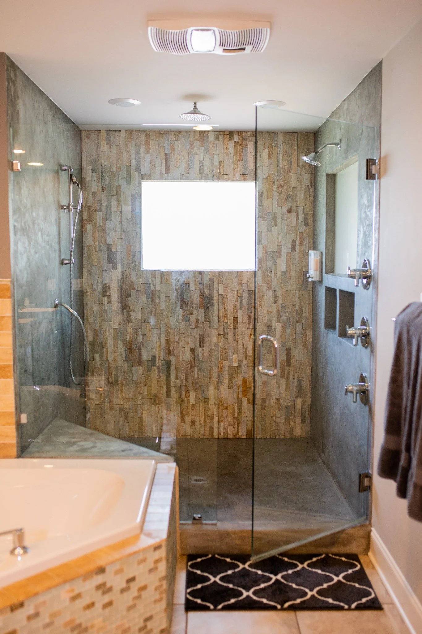 Main suite bathroom at the Manor onsite accommodation at Ramble Creek, featuring a spacious glass walk-in rain shower, stone tile walls, bathtub, and modern neutral finishes.