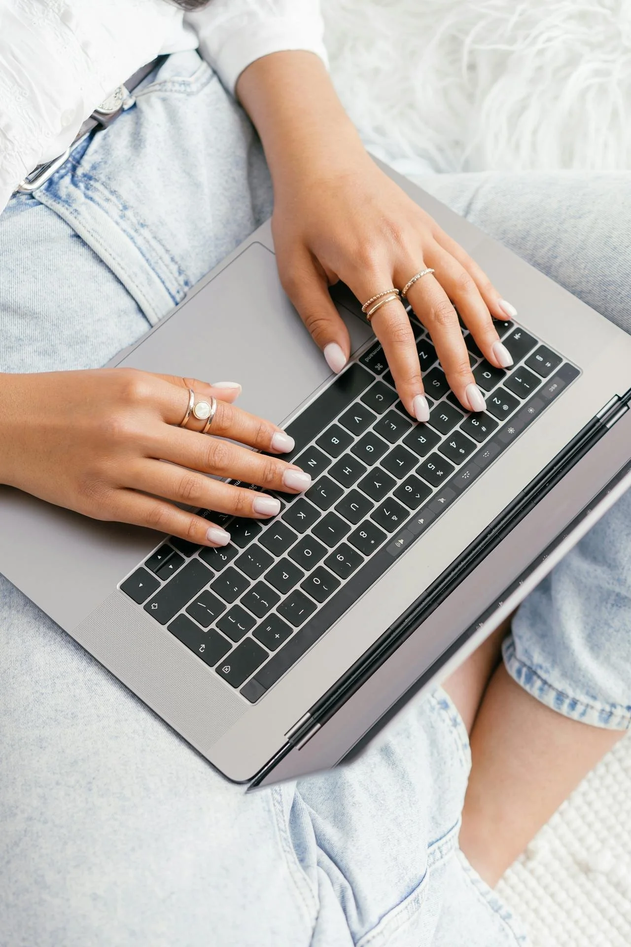 Person typing on a laptop keyboard, sitting with legs crossed in casual denim clothing filling out Ramble Creek pre-tour questionnaire.
