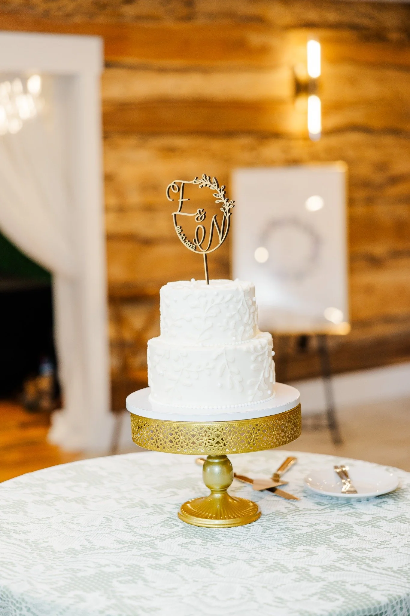 Two-tier white wedding cake on a gold stand with a custom monogram topper at Ramble Creek.