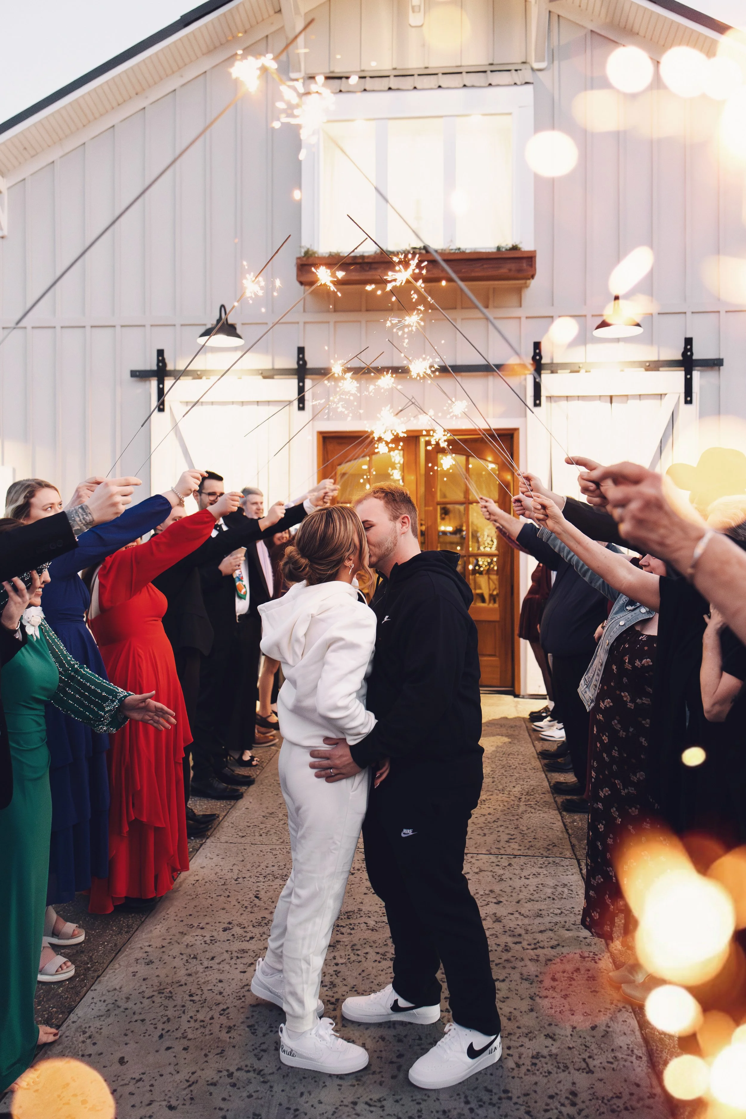 A romantic sparkler send-off outside the Grand Hall as the newlyweds share a kiss beneath glowing sparklers and warm evening lights, surrounded by cheering guests