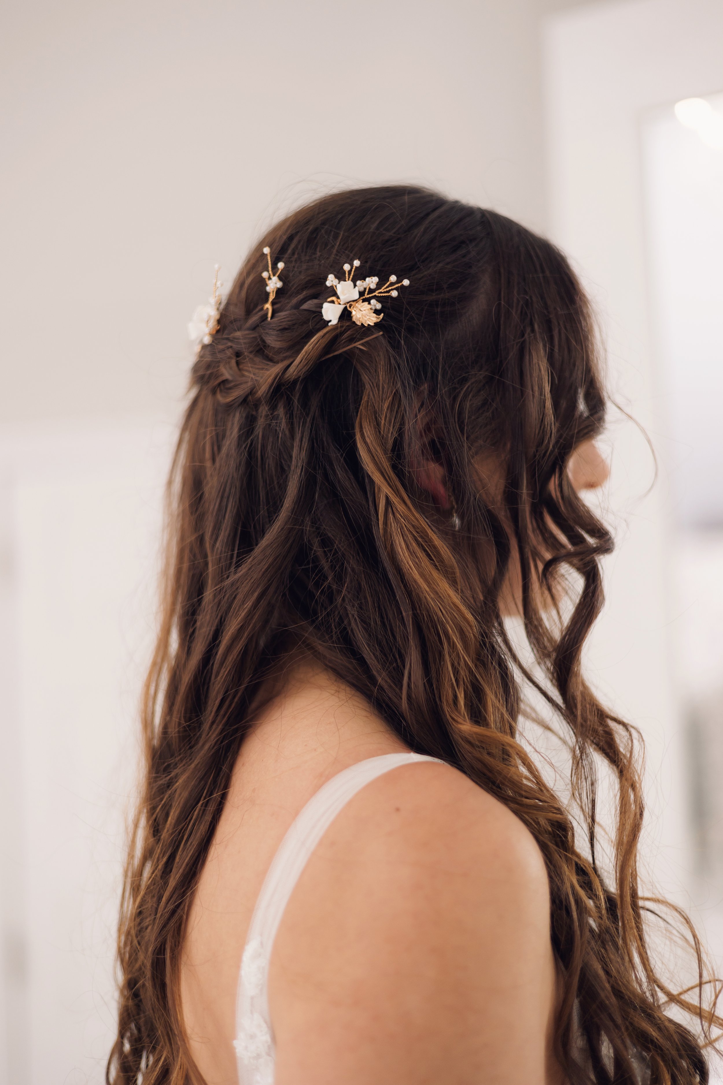Modern bridal half-up hairstyle with loose waves and delicate floral hair pins, creating a soft, romantic wedding look