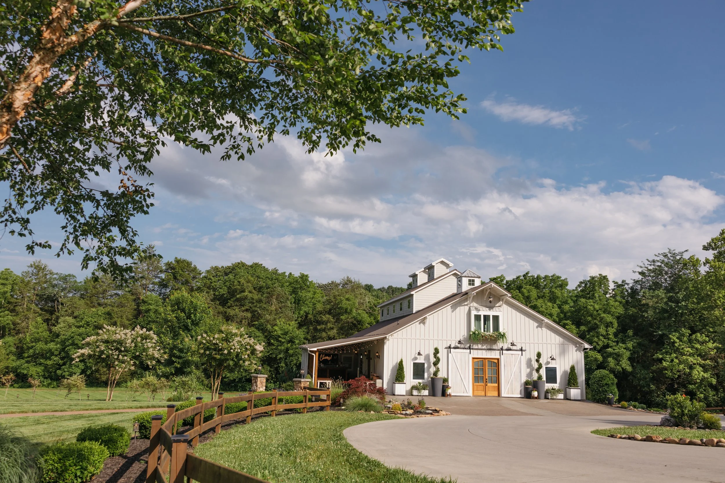 Ramble Creek all-inclusive wedding venue exterior in Tennessee with white siding, wood doors, landscaped grounds, and a tree-lined driveway under a blue sky