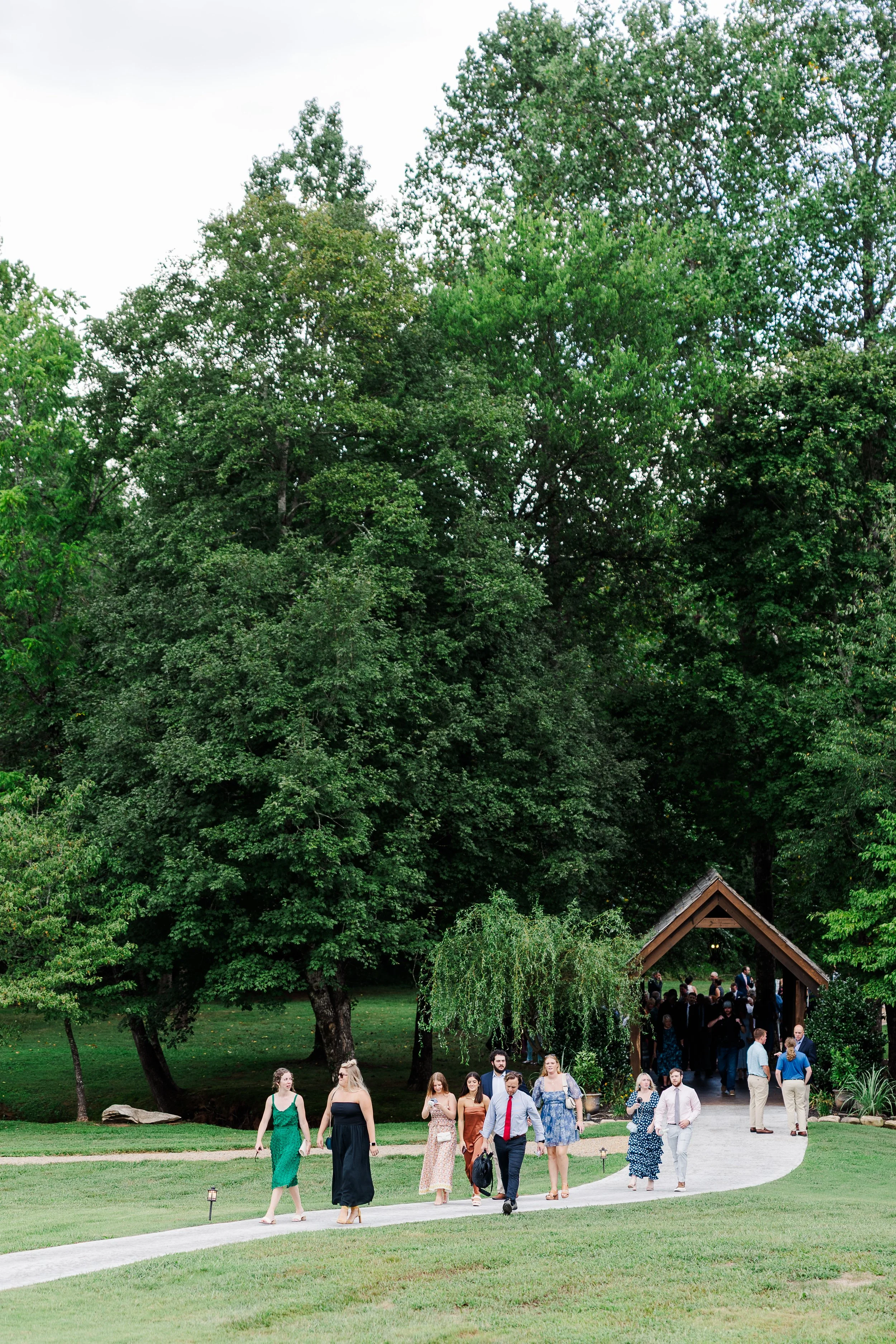 Wedding guests walking from Ramble Creek’s outdoor ceremony area through a lush Tennessee landscape after a summer wedding.