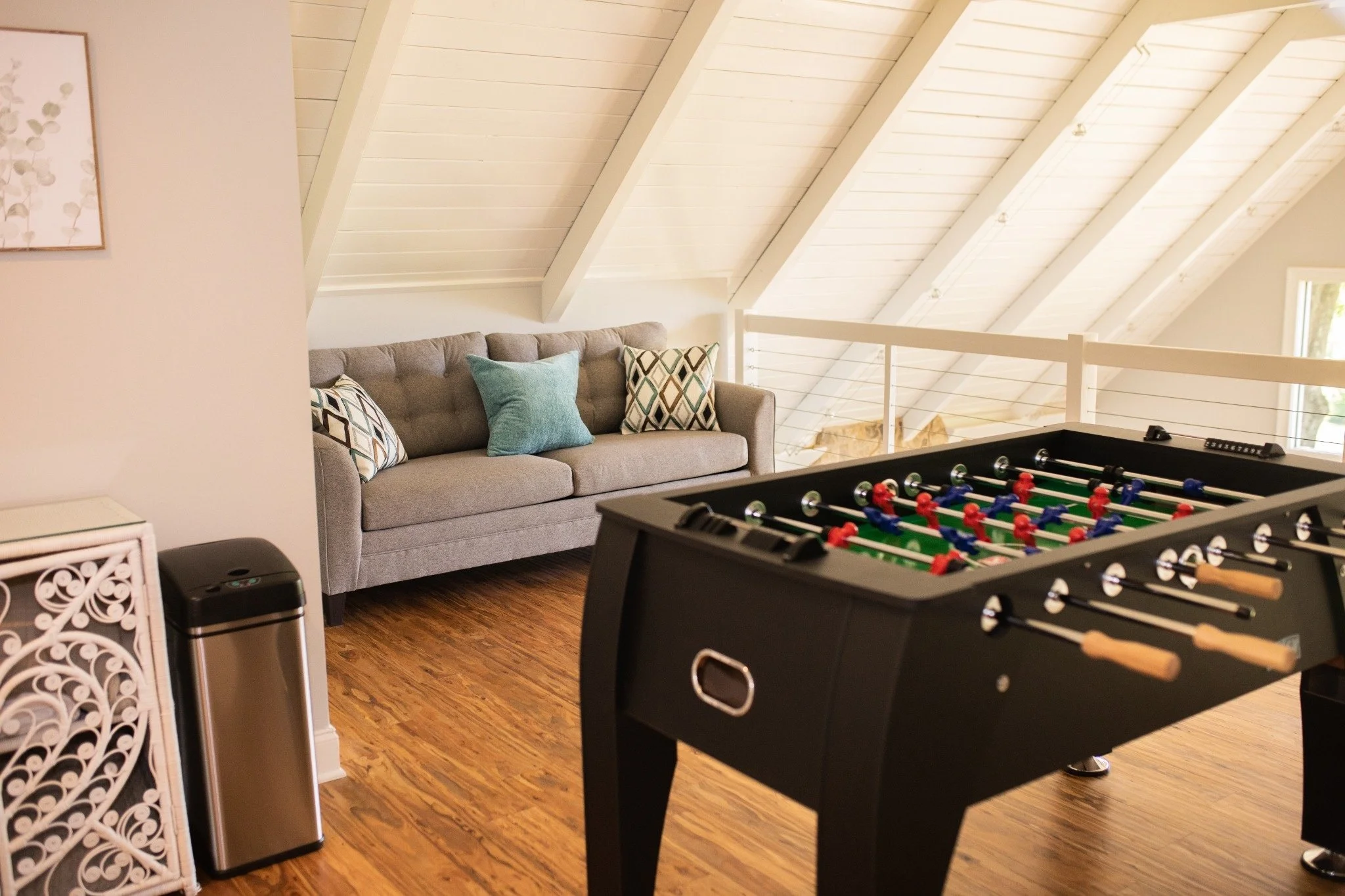 Game loft at the Manor onsite accommodation at Ramble Creek, featuring a foosball table, cozy sofa seating, vaulted ceilings, and warm wood floors.