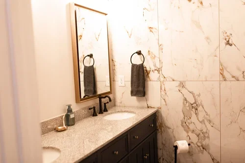 Bathroom inside the Villa at Ramble Creek, featuring a dark vanity, stone countertop, large mirror, marble-style tile walls, and neutral finishes.