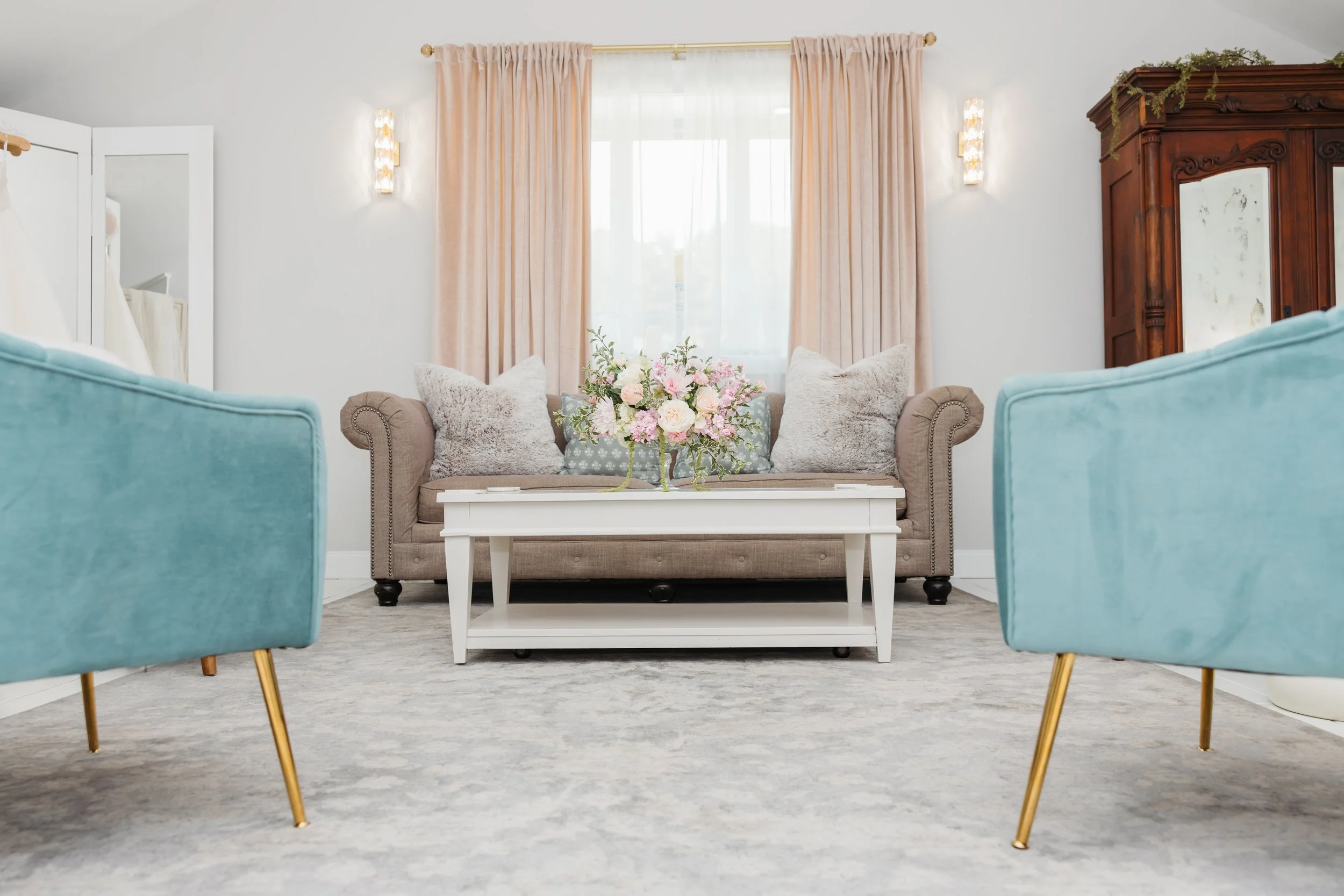 Ramble Creek bridal suite with a beige sofa, floral centerpiece on a white coffee table, pink curtains, and blue armchairs with gold legs.