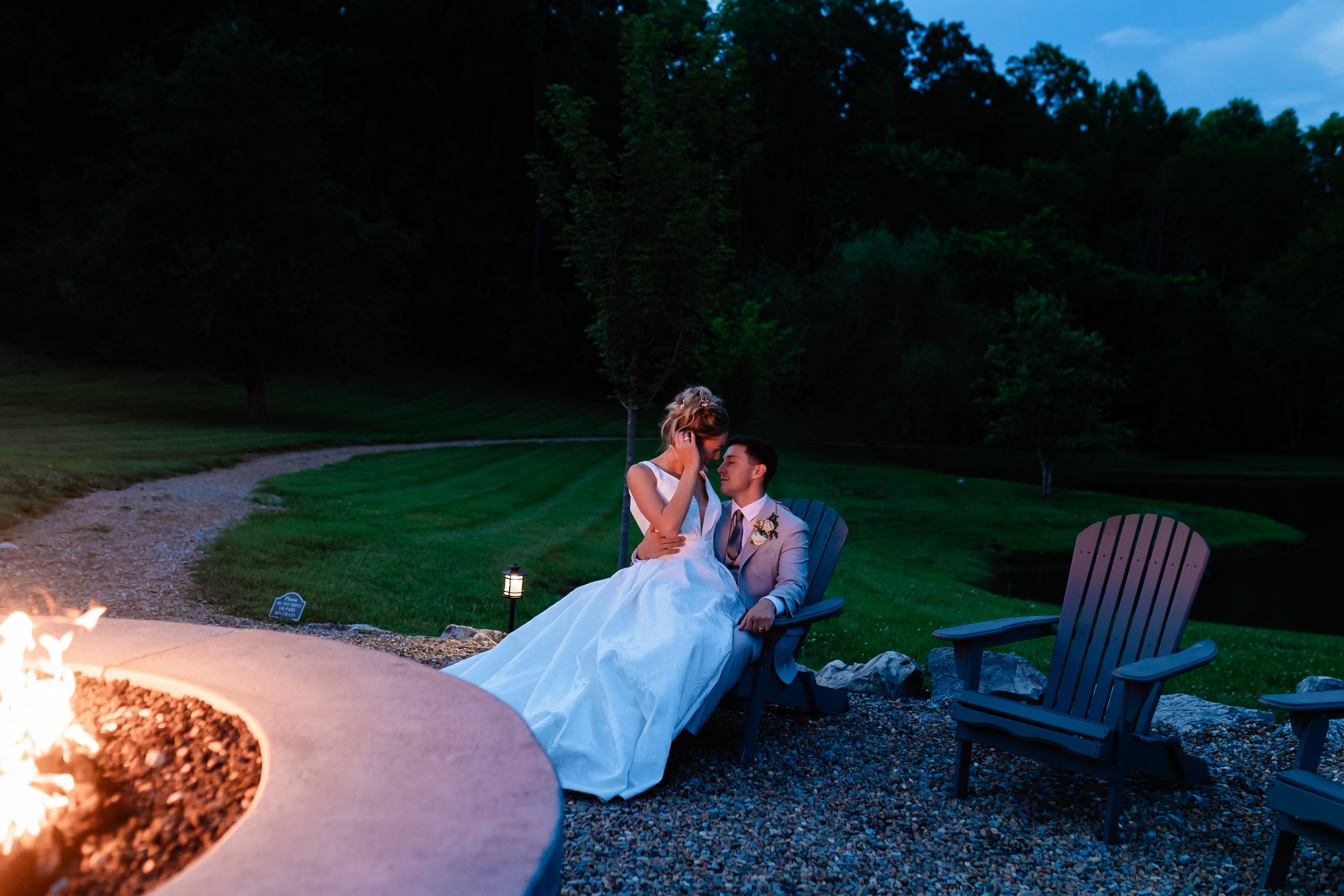 Bride and groom share a quiet nighttime moment by the firepit at Ramble Creek after their outdoor wedding celebration.
