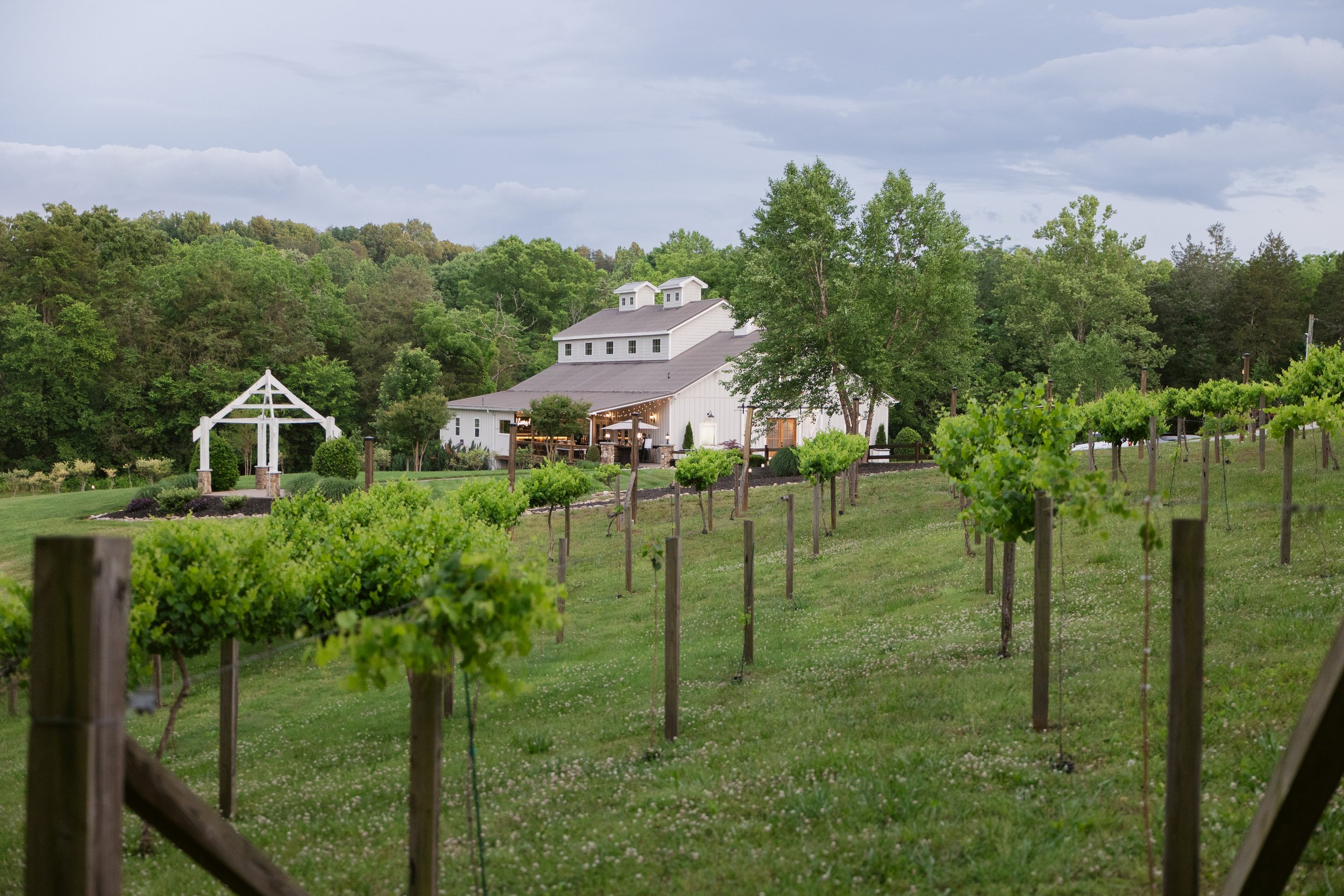A white, natural feeling wedding venue in East Tennessee with a gray roof surrounded by trees and a vineyard.