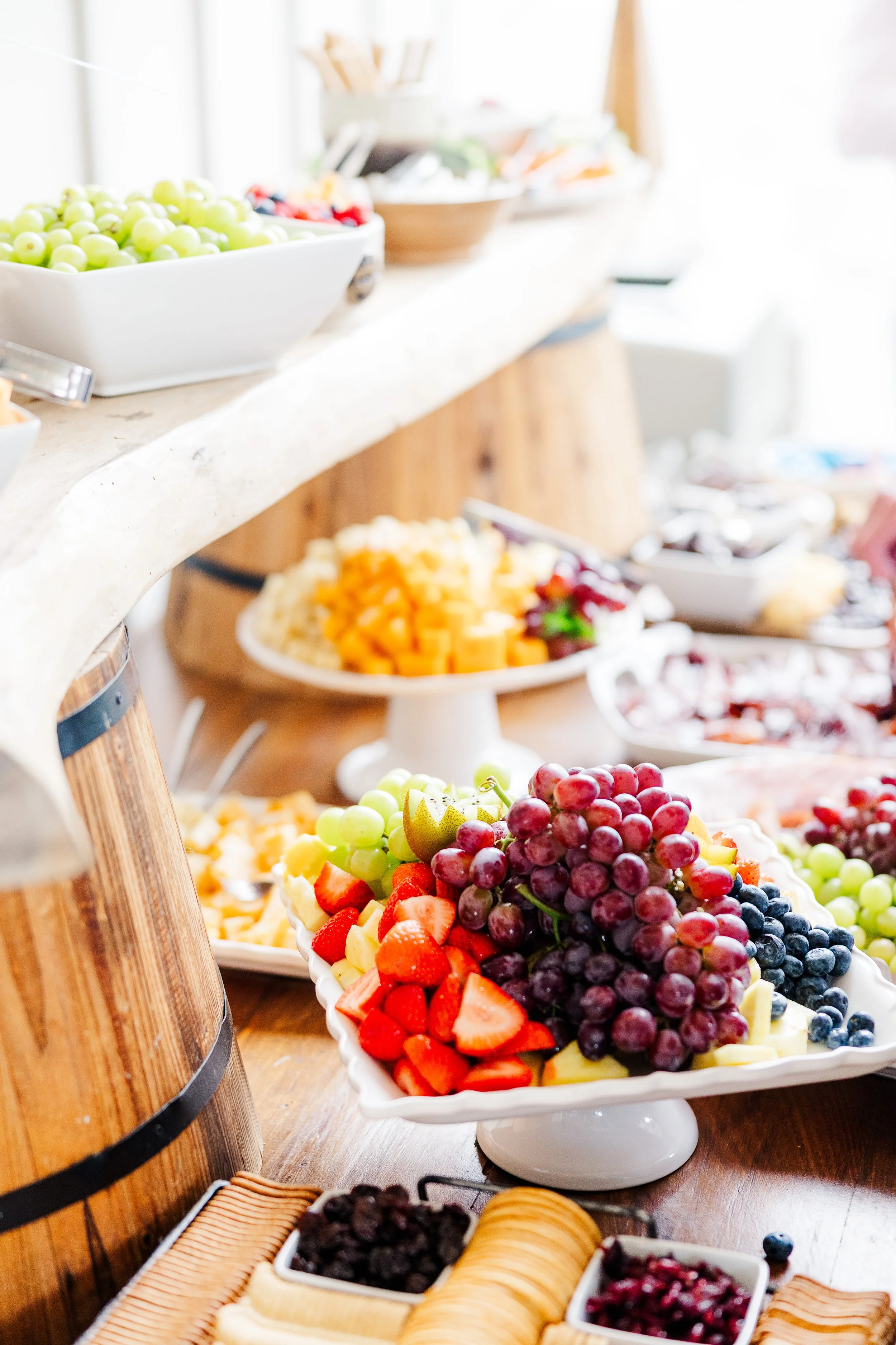 Arrangement of fruit on a buffet table, featuring grapes, strawberries, blueberries, and diced melons in white dishes during Ramble Creek wedding cocktail or social hour.