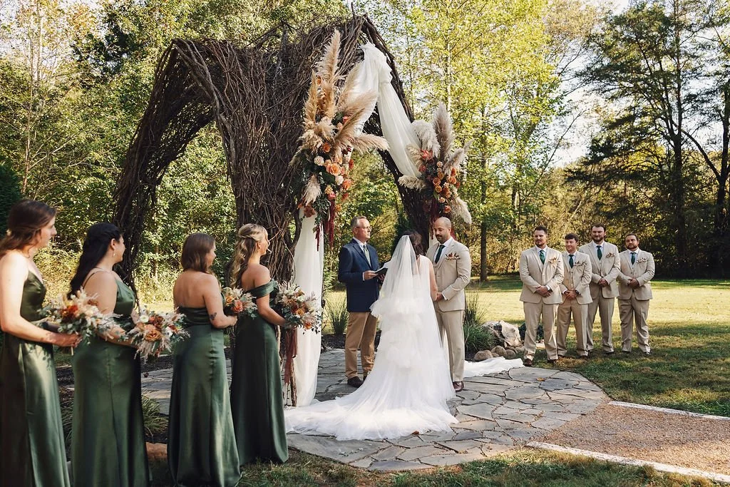 Outdoor wedding ceremony under vine arbor with floral arrangements at Ramble Creek Tennessee wedding venue