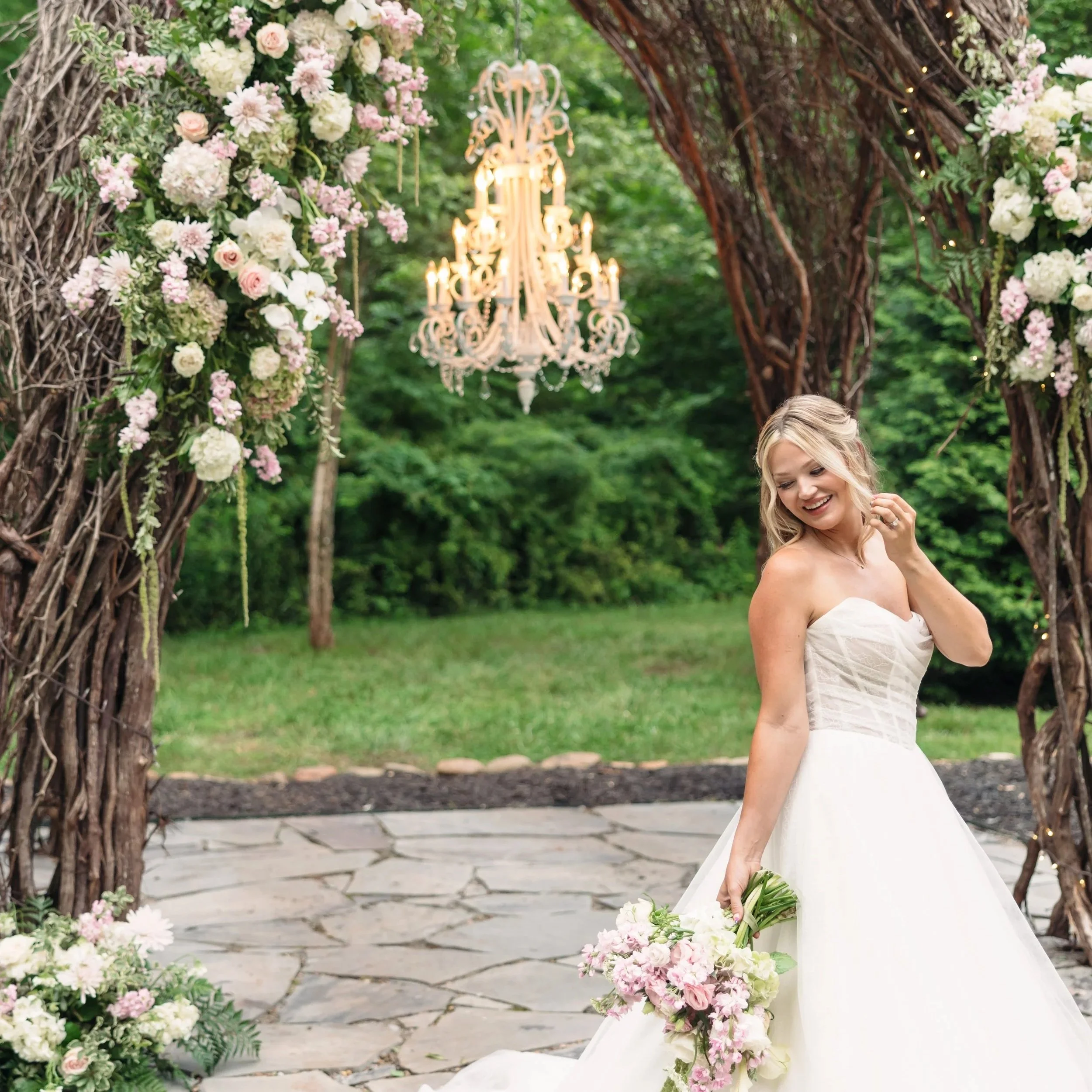 Smiling bride beneath outdoor vine arbor at Ramble Creek all-inclusive wedding venue, holding pink spring florals
