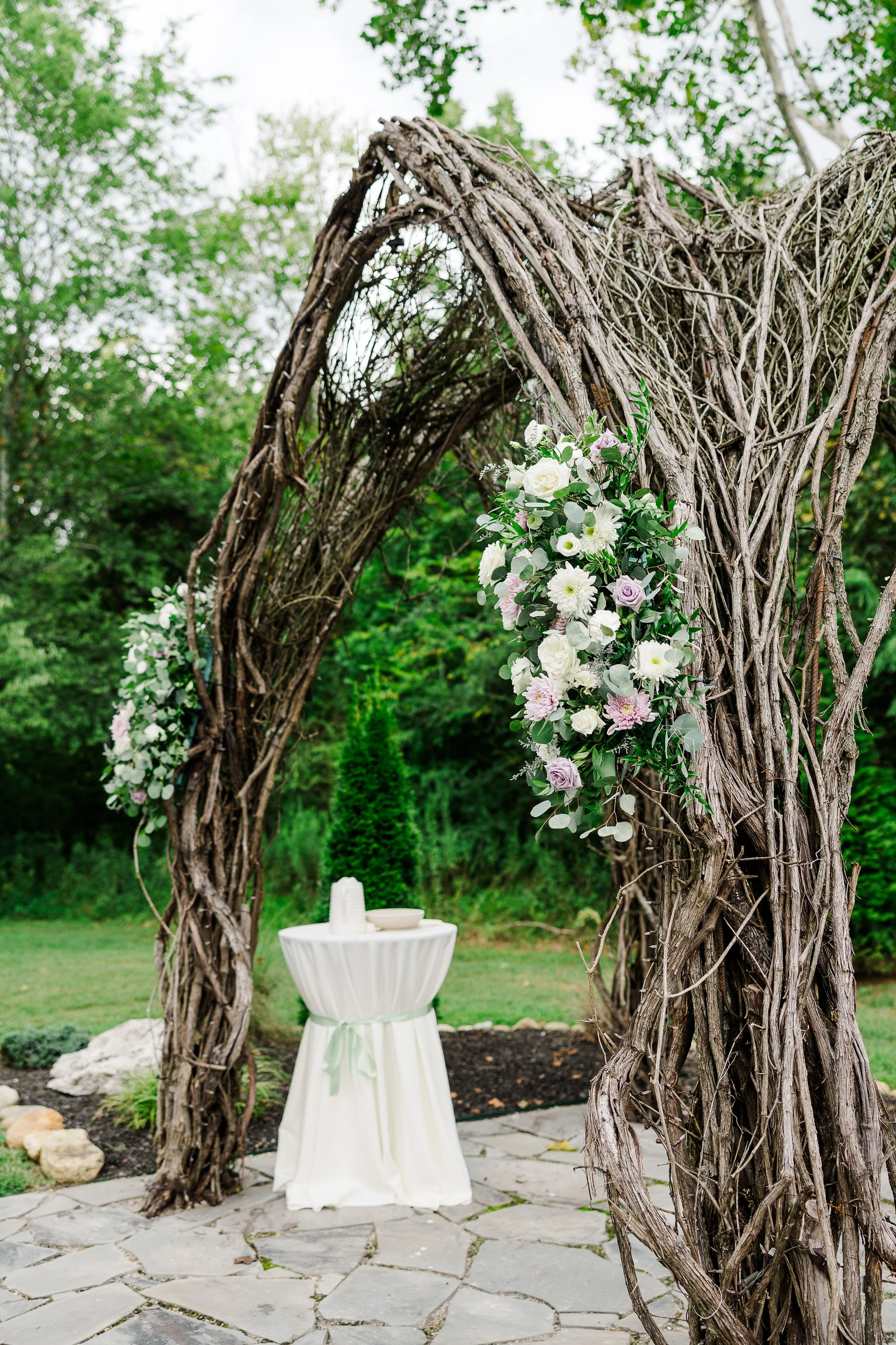 Close-up of Ramble Creek’s natural vine arbor with white and lavender floral arrangements for a romantic outdoor Tennessee summer wedding ceremony.