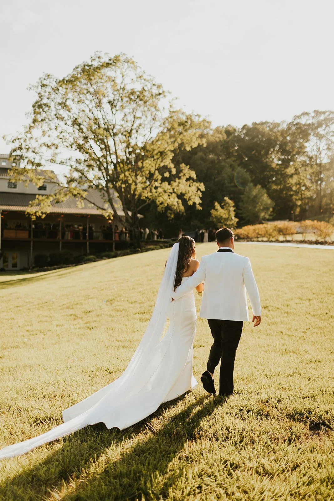 Bride and groom walking across Ramble Creek’s sunlit lawn during a golden hour summer wedding in Tennessee.
