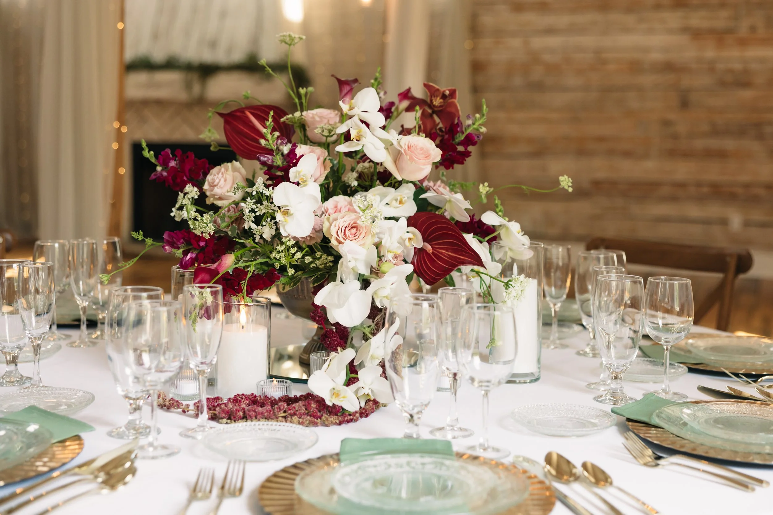 Elegant wedding reception table at Ramble Creek with a burgundy, blush, and white floral centerpiece, candles, glassware, and layered place settings.