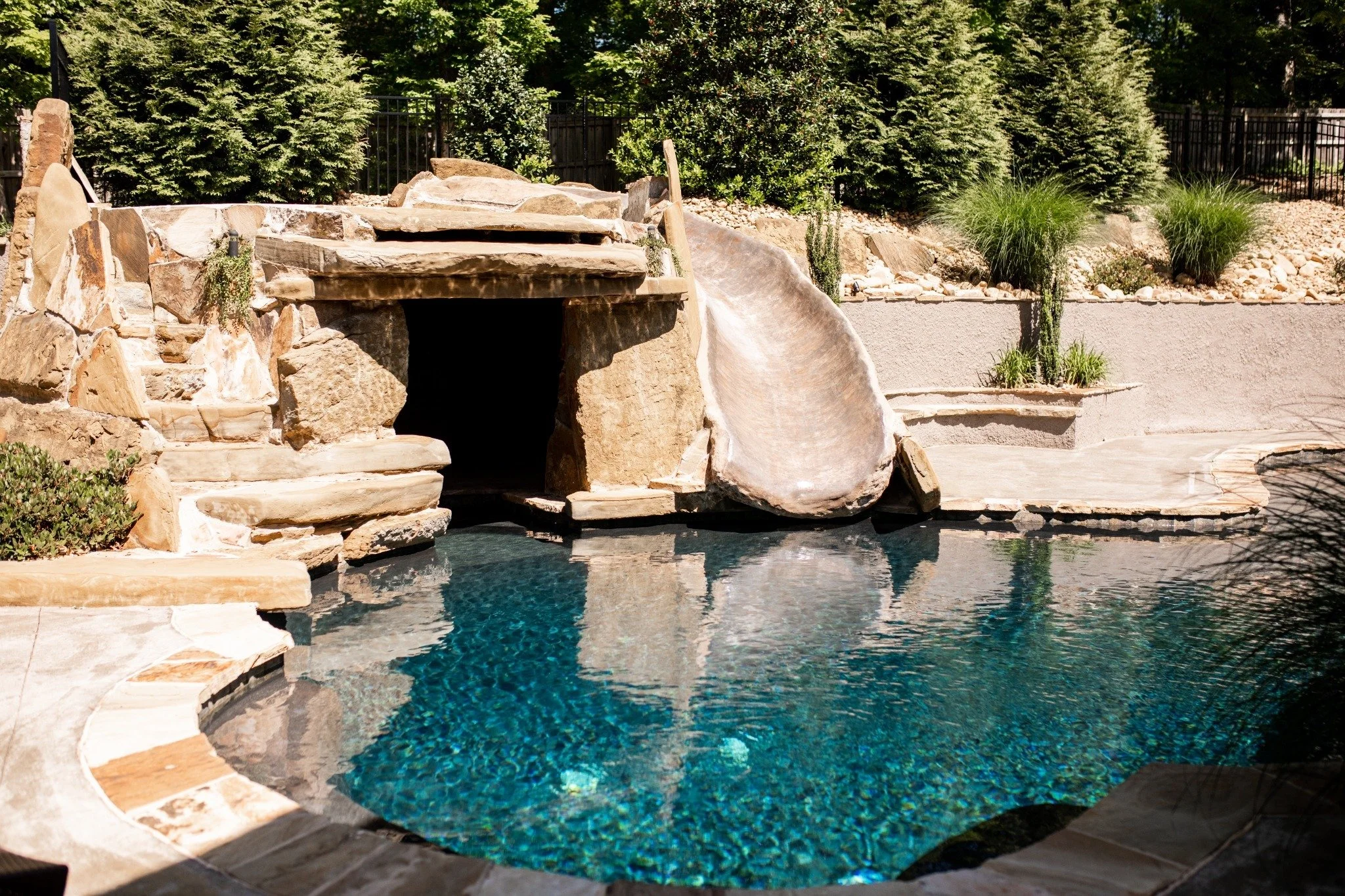 Stone pool with a built-in waterslide, waterfall feature, and landscaped greenery at Ramble Creek’s onsite Manor accommodation.