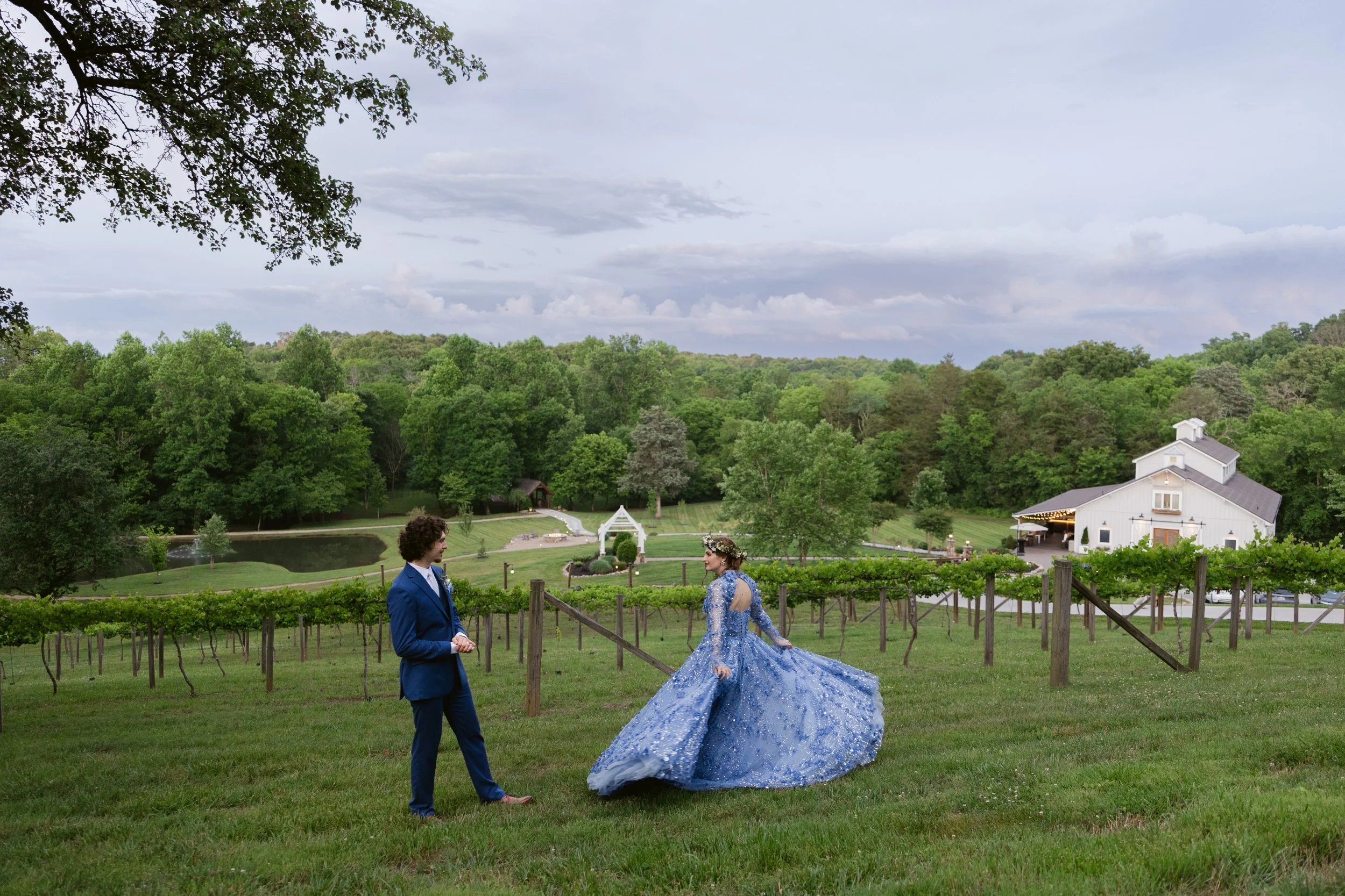 Bride in a blue floral wedding dress and groom in a blue suit overlooking the vineyard and grounds at Ramble Creek, an all-inclusive East Tennessee wedding venue in Athens TN.