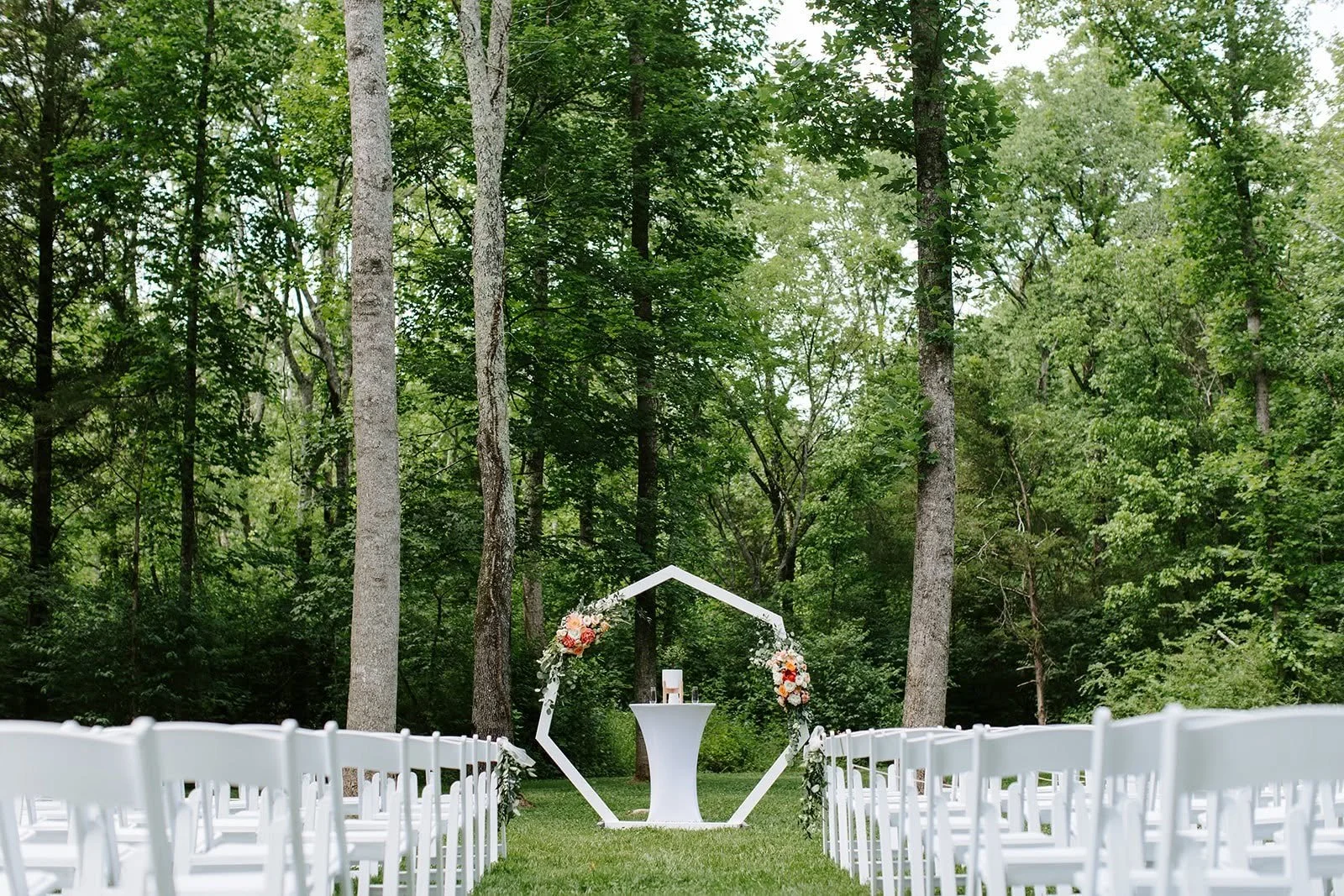 Bride and groom kissing beneath a floral arbor at Ramble Creek, with a white cross visible in the background of the outdoor ceremony space