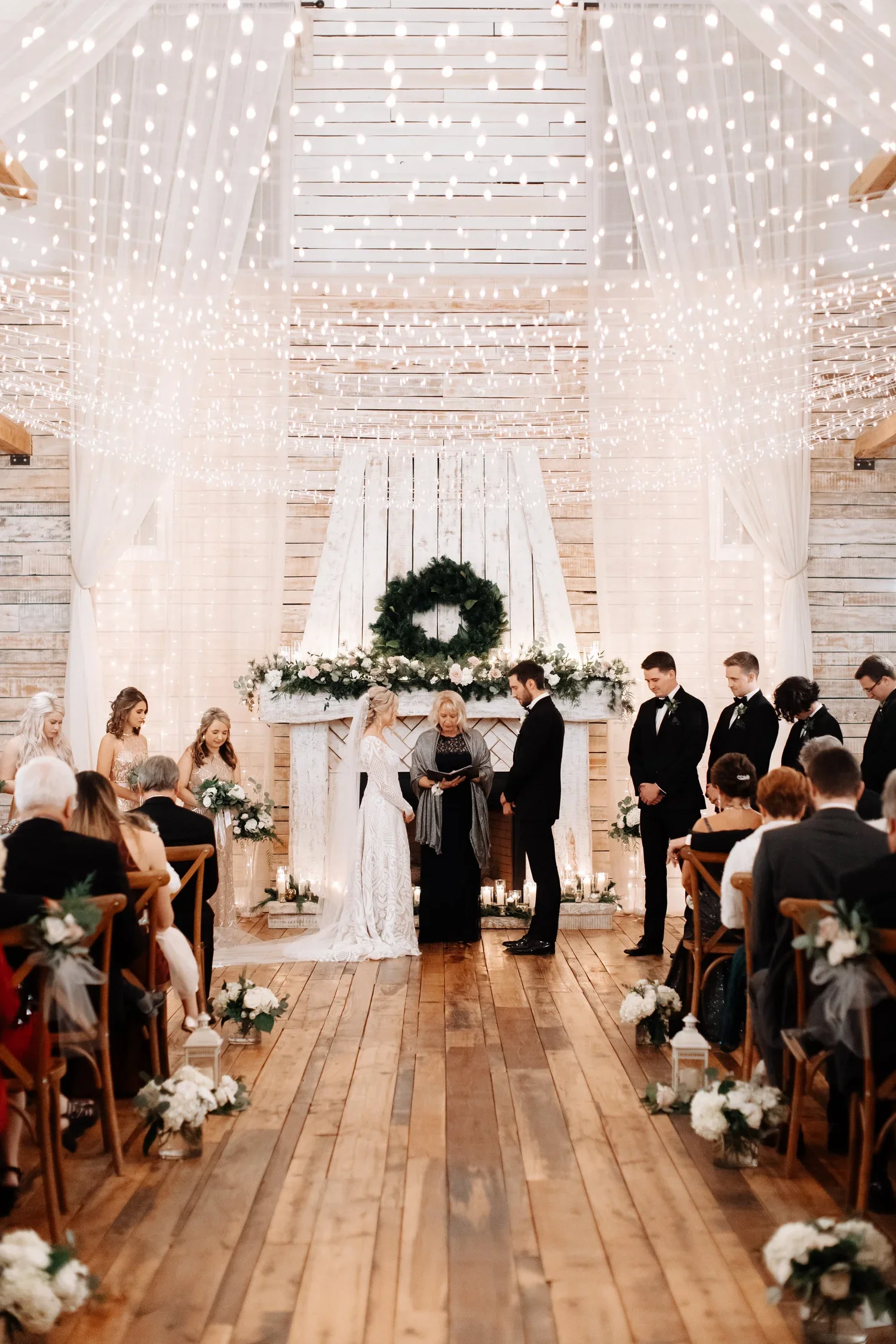 Indoor Ramble Creek wedding ceremony with twinkle lights, white draping, greenery, and candlelit aisle decor