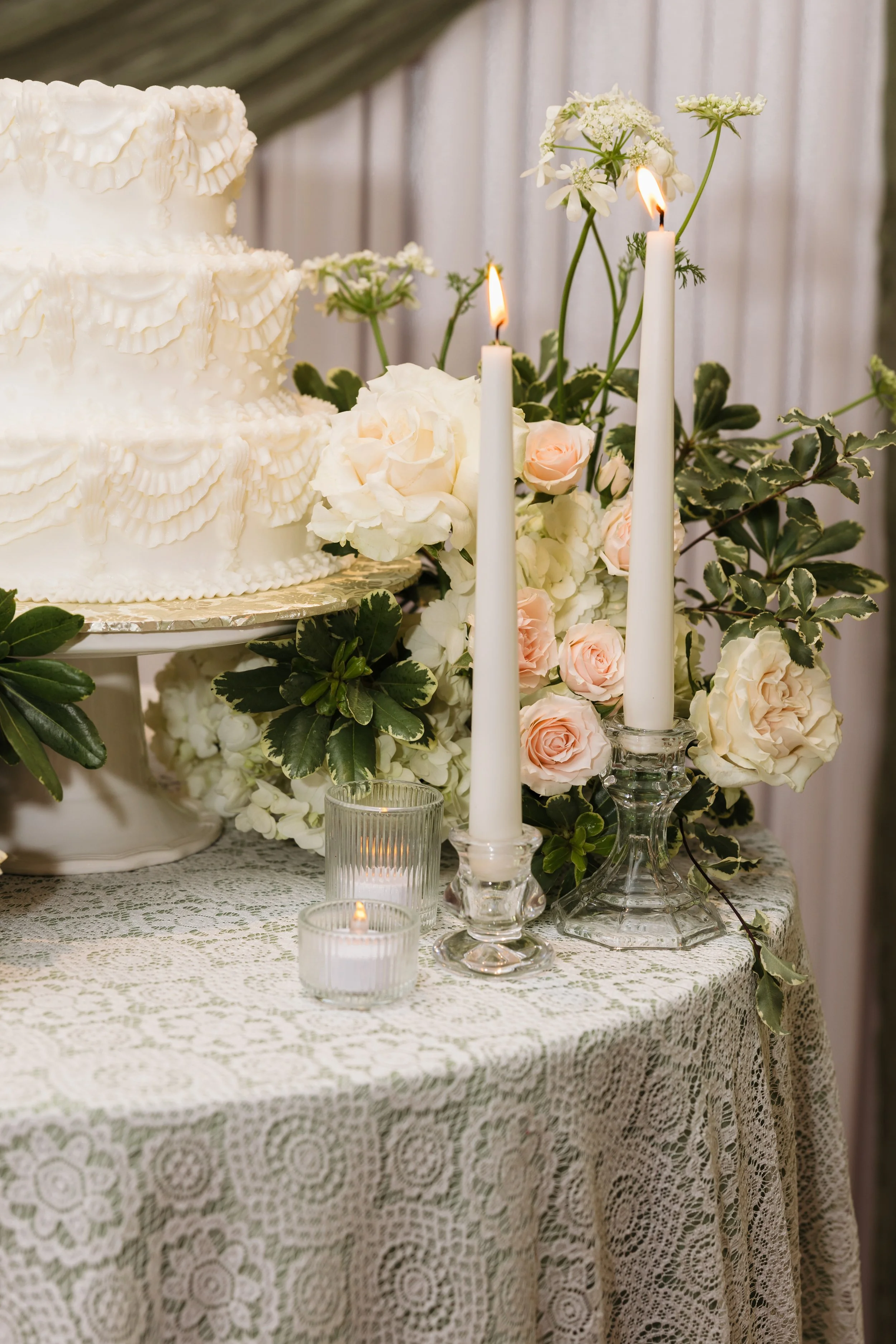 White wedding cake detail at Ramble Creek with soft blush and ivory florals, candlelight, lace linens, and elegant reception décor