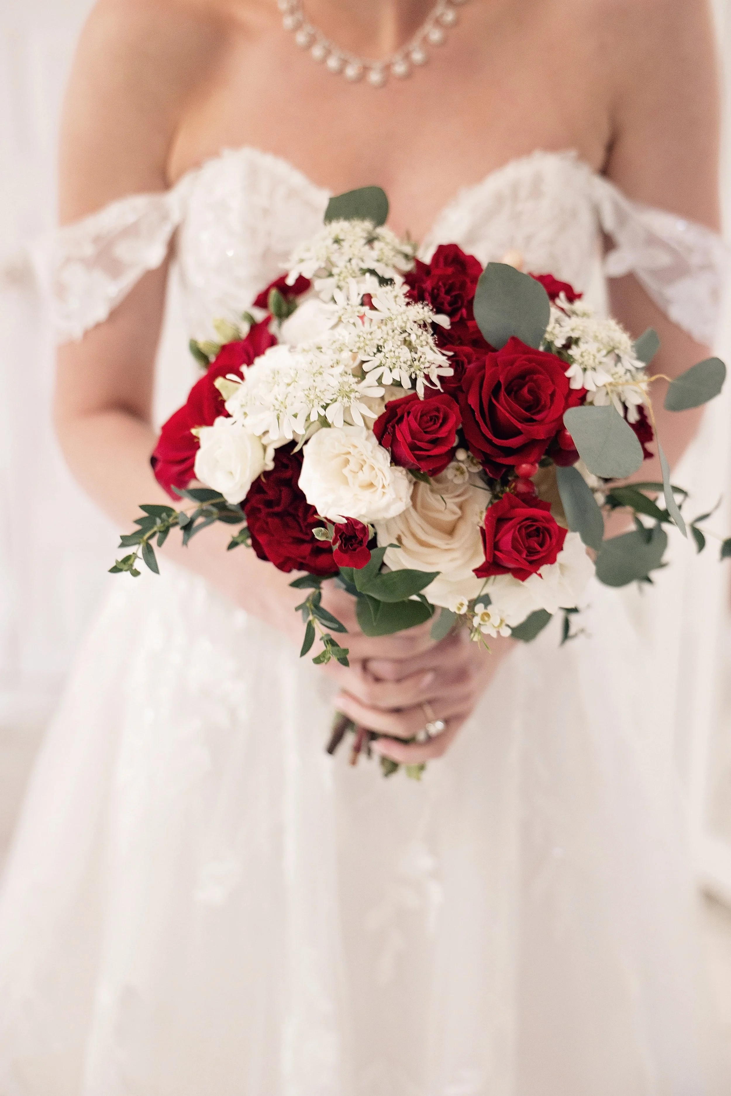A bride in a white wedding dress holding a bouquet of red, white, and green flowers.