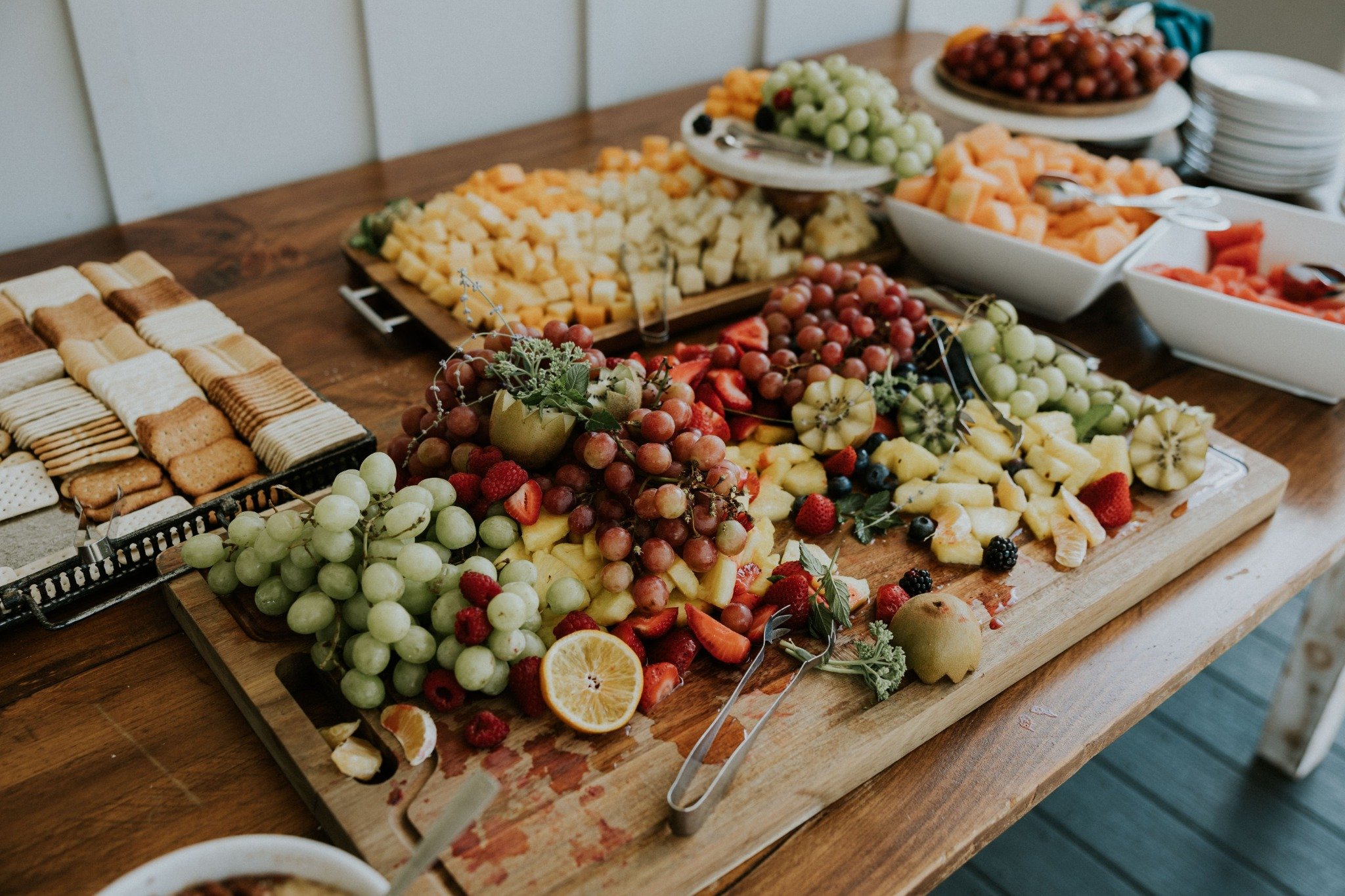 Wedding reception fruit and cheese display at Ramble Creek, featuring grapes, berries, sliced fruit, cheeses, crackers, and serving dishes arranged on a wooden table.