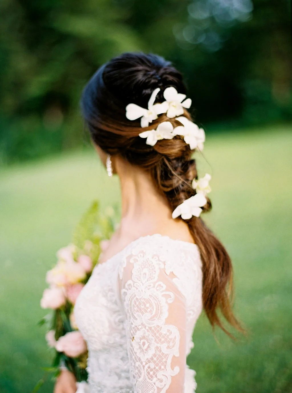 Bride wearing a romantic floral bridal hairstyle with white blooms woven into a soft ponytail, paired with a lace wedding dress at Ramble Creek.