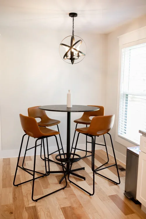 Kitchen seating nook inside the Villa at Ramble Creek, featuring a round bistro table, tan bar chairs, globe pendant light, and bright window.